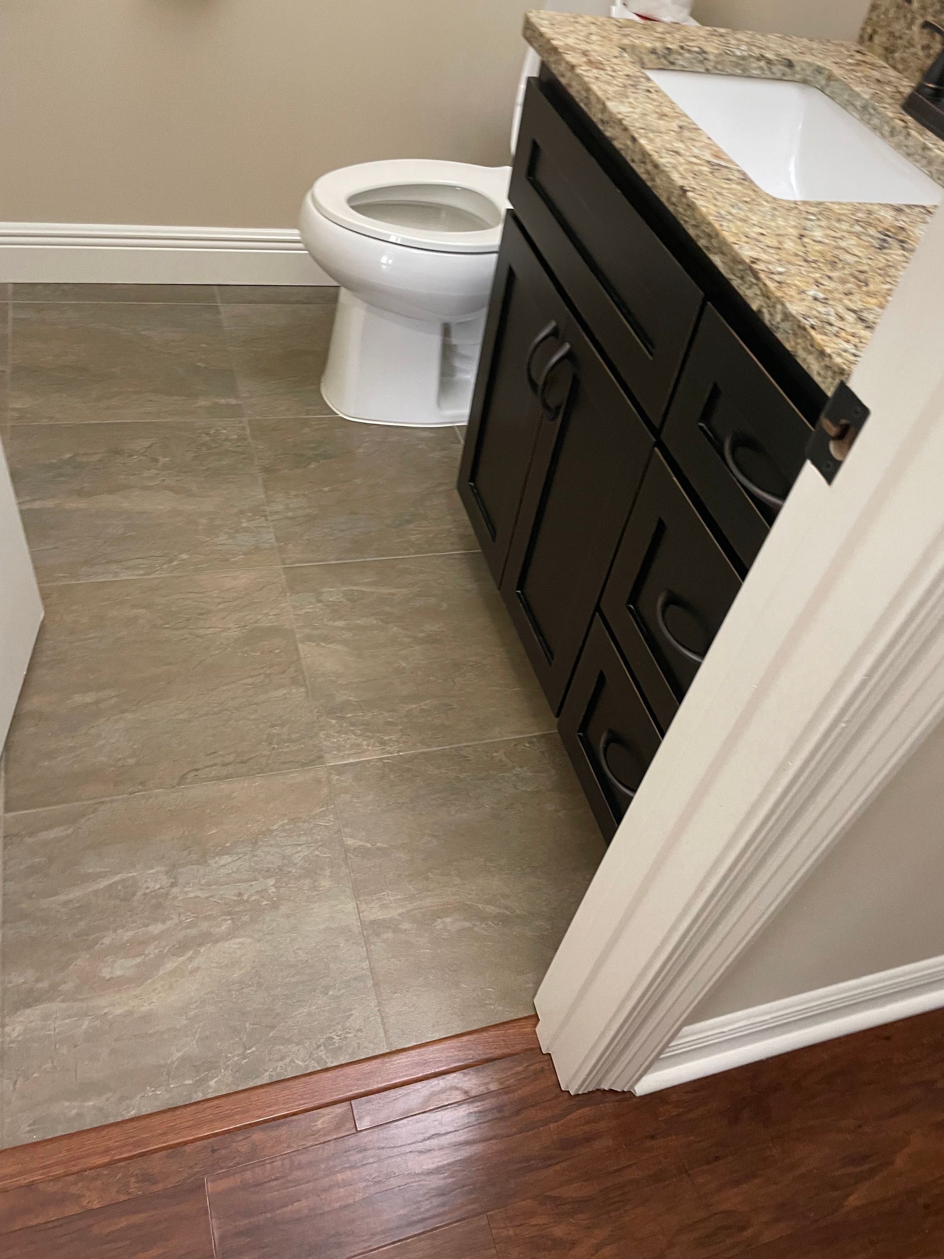 Bathroom with toilet, vanity cabinet, and granite countertop beside a doorway and wood threshold.