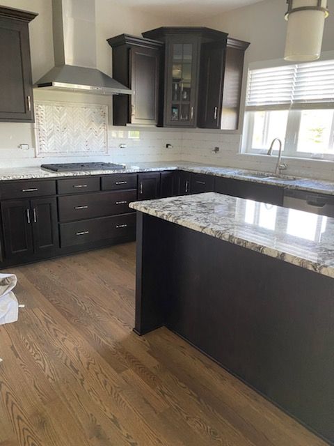 Modern kitchen with dark cabinets, granite island, stainless range hood, and hardwood floors