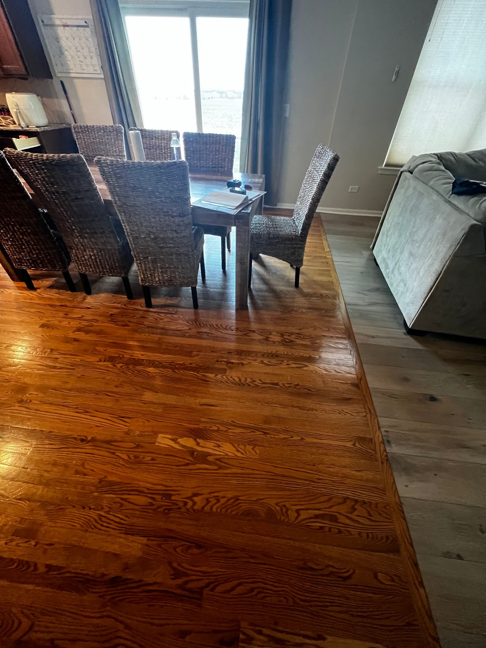 Dining area with wicker chairs, glass table, hardwood floor, and a bright window by a radiator.
