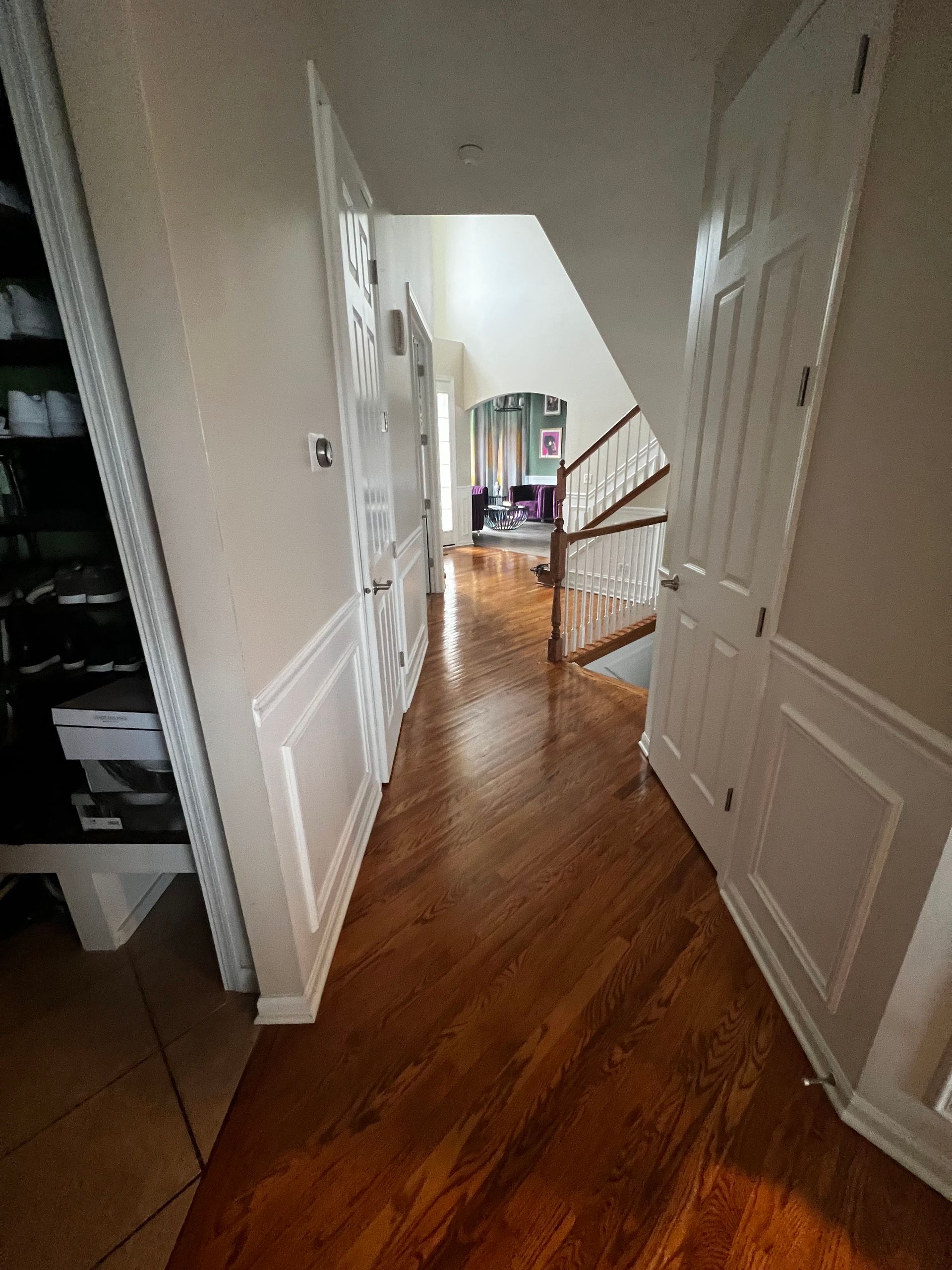 Narrow hallway with wood floors, white walls, and stairs leading to a bright room at the end.