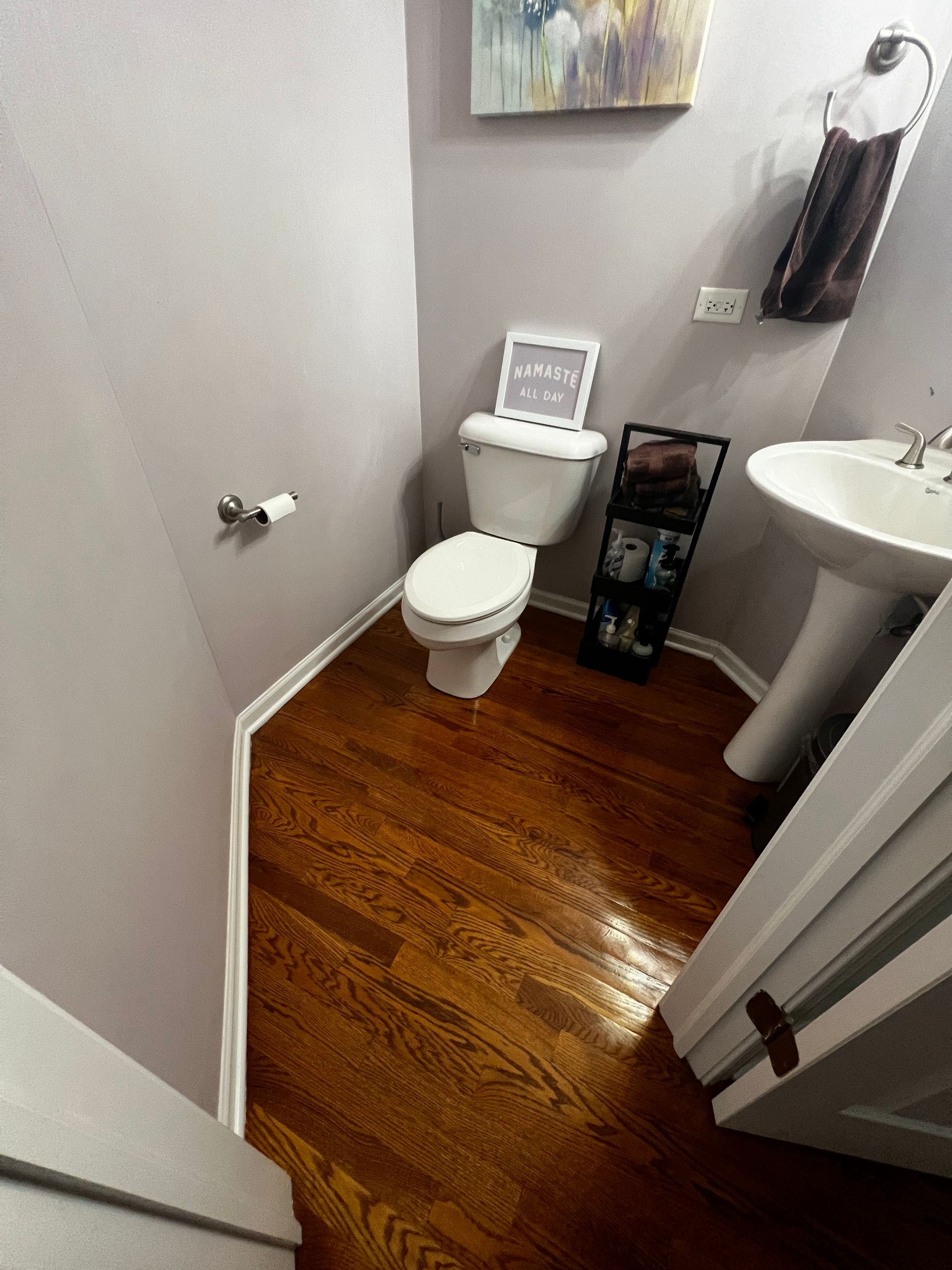 Small bathroom with toilet, pedestal sink, white walls, and wood-pattern floor.