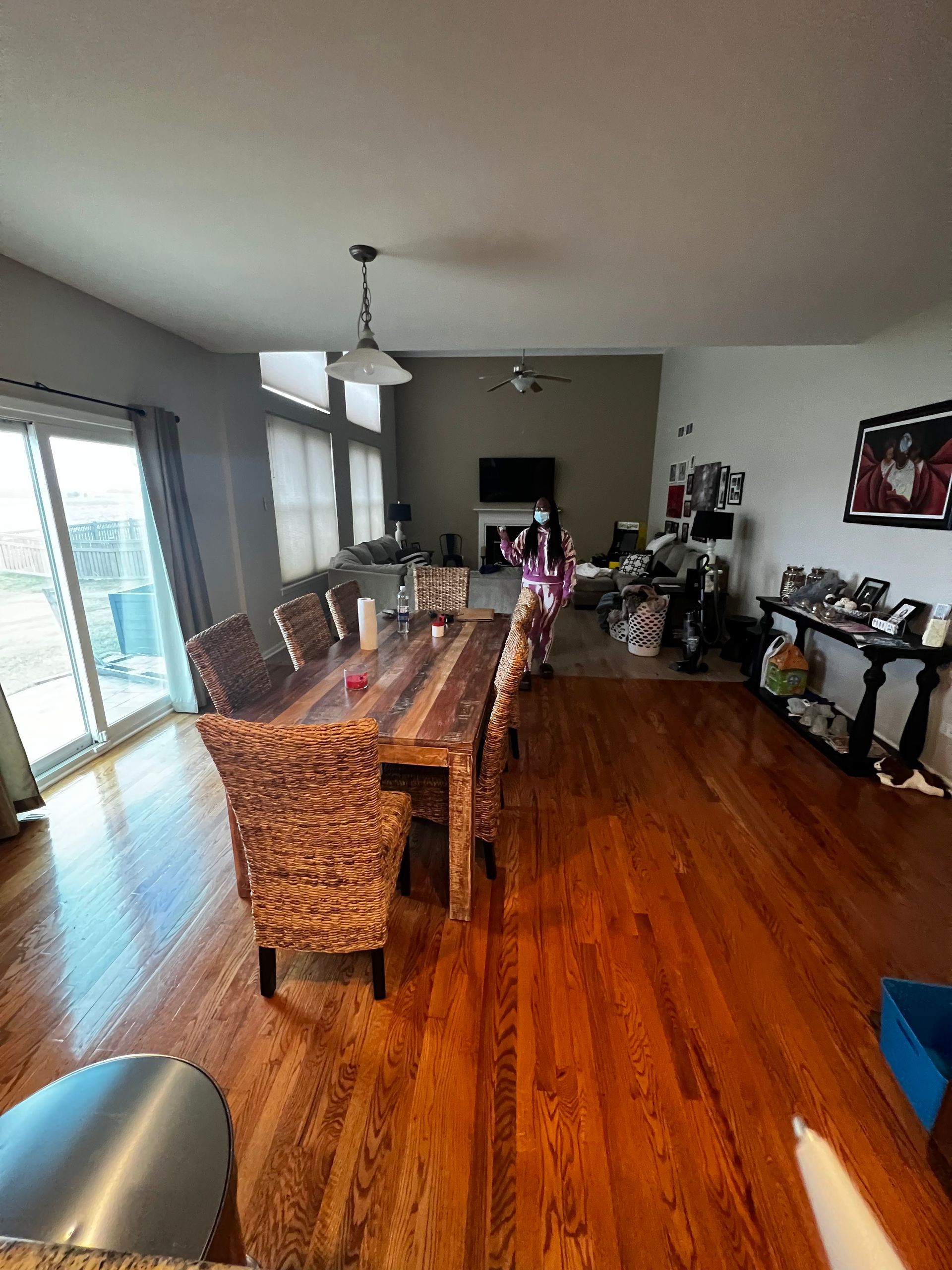 Dining room with long wooden table, wicker chairs, and hardwood floors beside a sliding glass door.