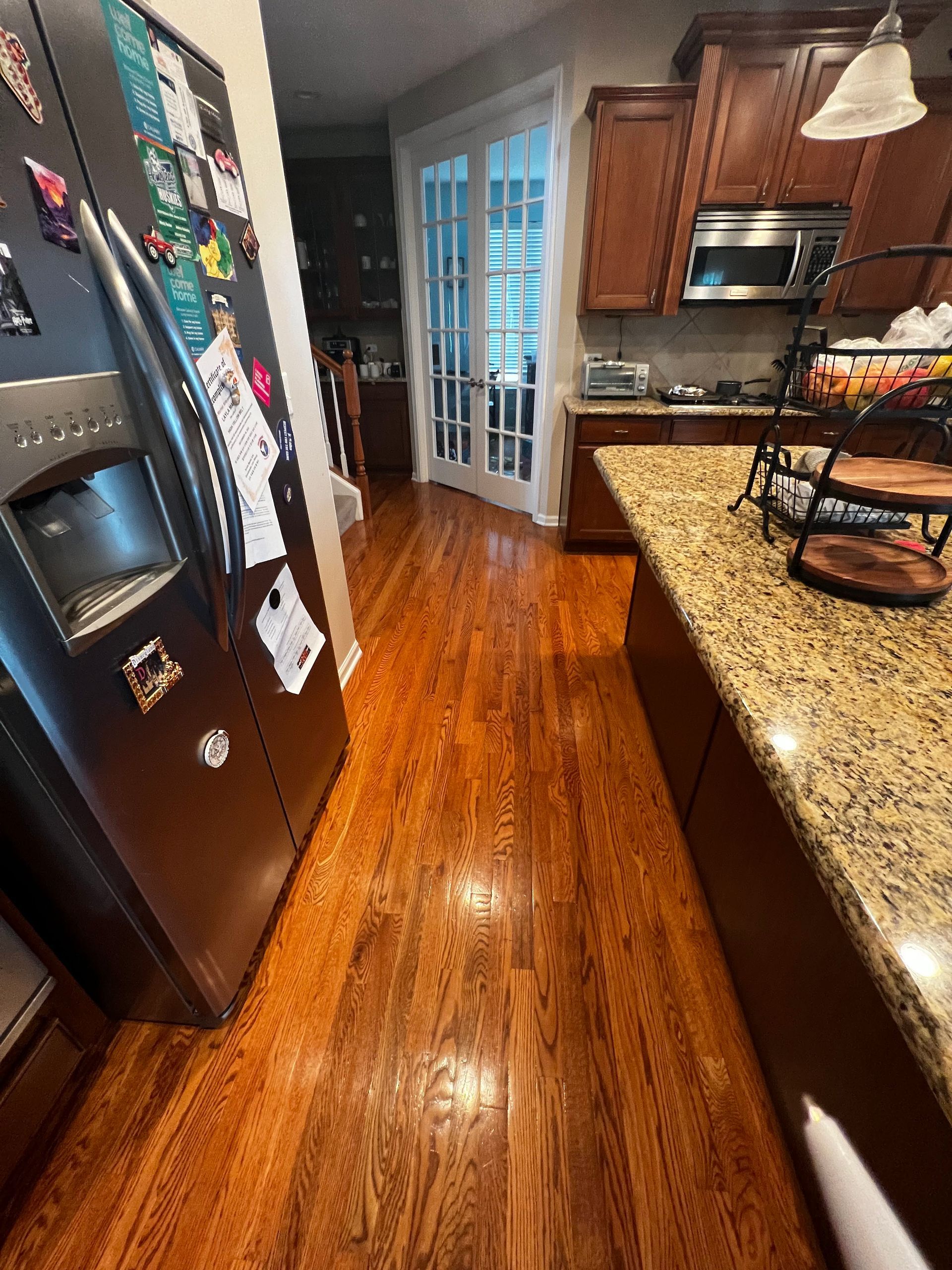 Modern kitchen with hardwood floors, black refrigerator, granite island, and sliding glass doors.