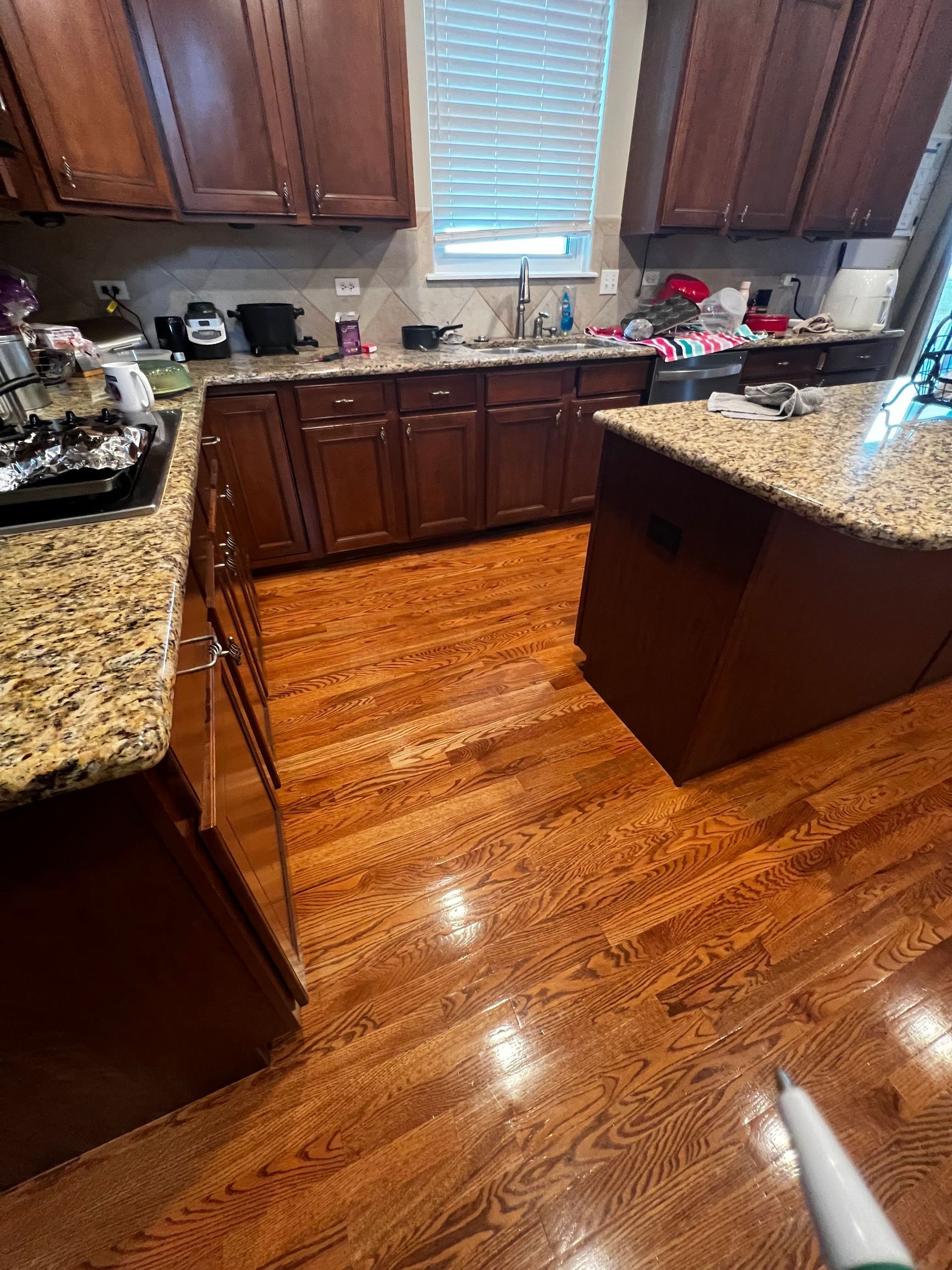 Spacious kitchen with dark wood cabinets, granite counters, and a shiny hardwood floor.
