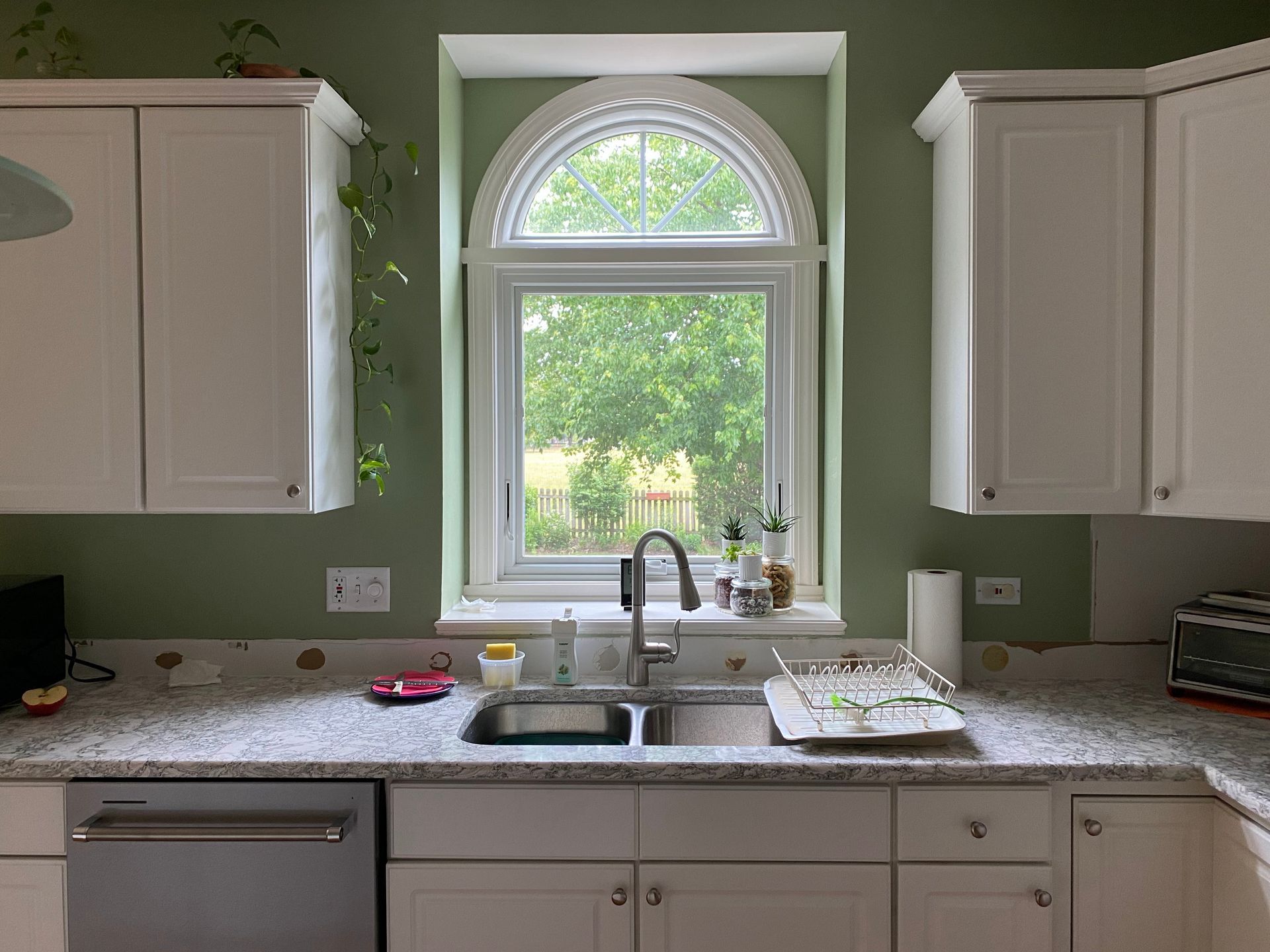 Bright kitchen sink under arched window with white cabinets and green walls