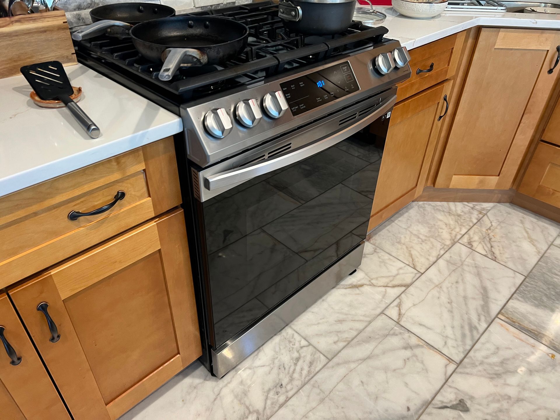 Black gas range oven in a kitchen with wooden cabinets and marble tile floor.