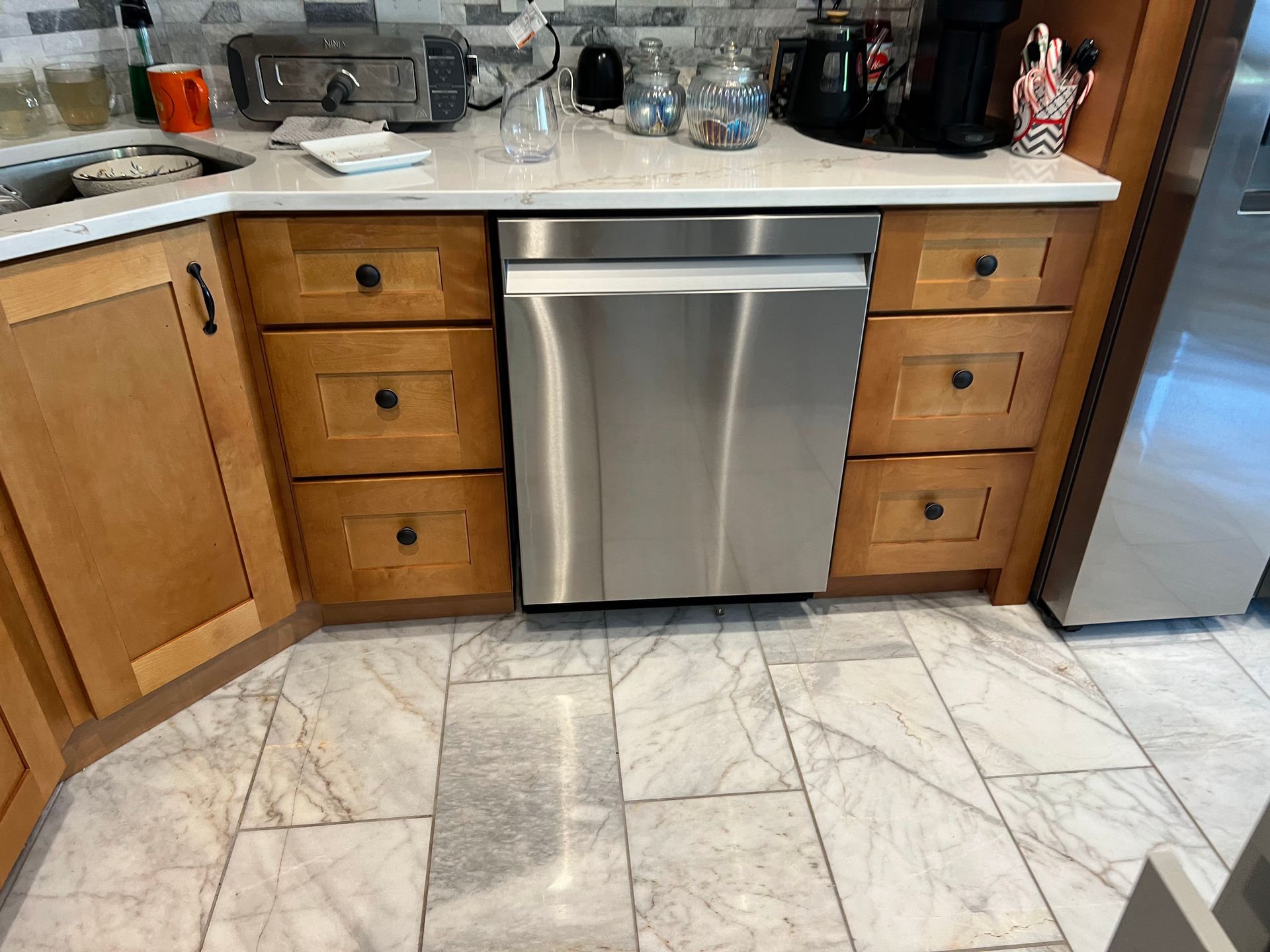 Kitchen with stainless steel dishwasher, wooden cabinets, and marble-pattern tile floor.