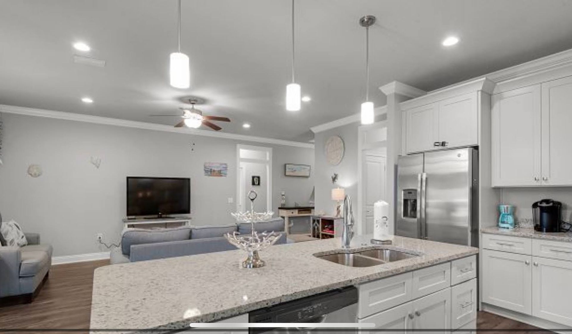 Bright, modern kitchen with white cabinets, granite island, and stainless steel appliances, open to a living room