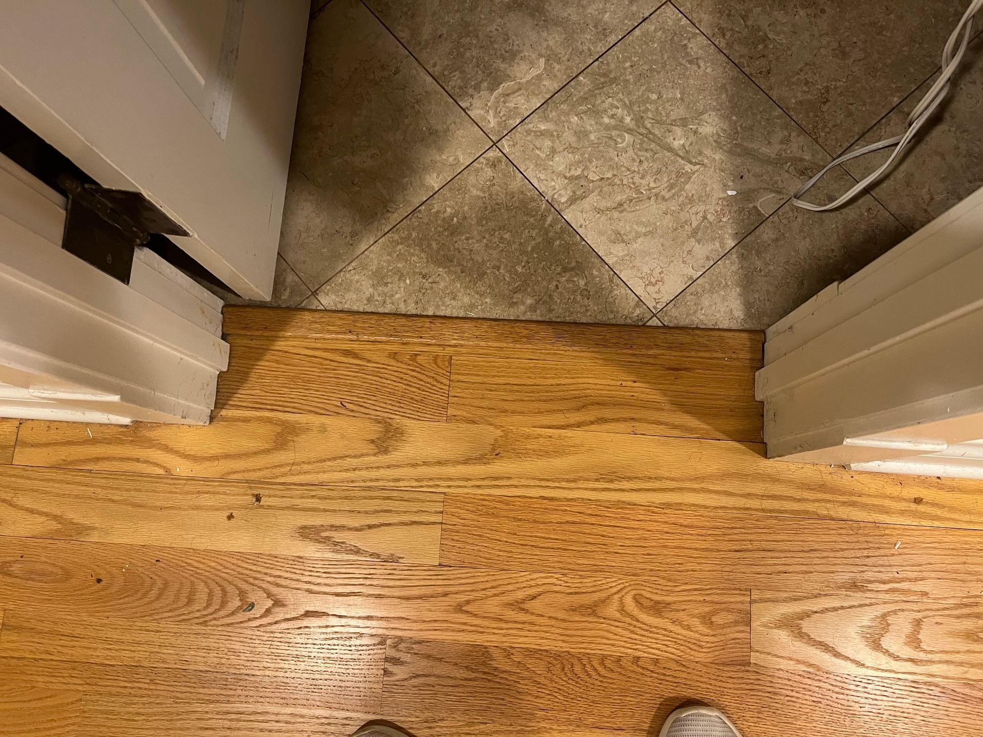 Threshold between hardwood floor and tiled entryway with a cord on the right side.