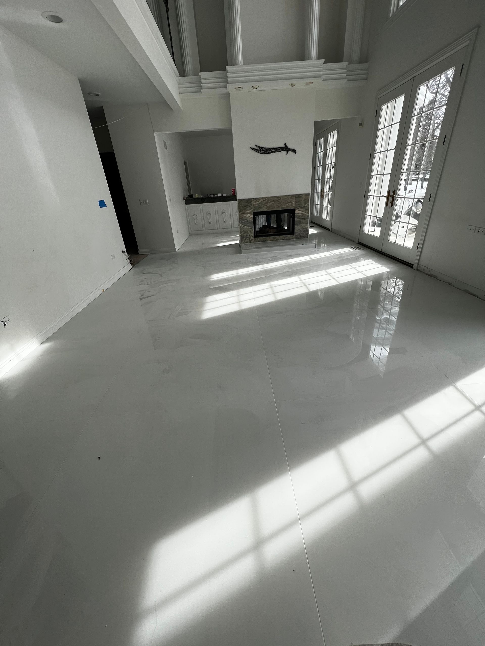 Empty modern living room with glossy white floor, sunlight streaming through large windows.