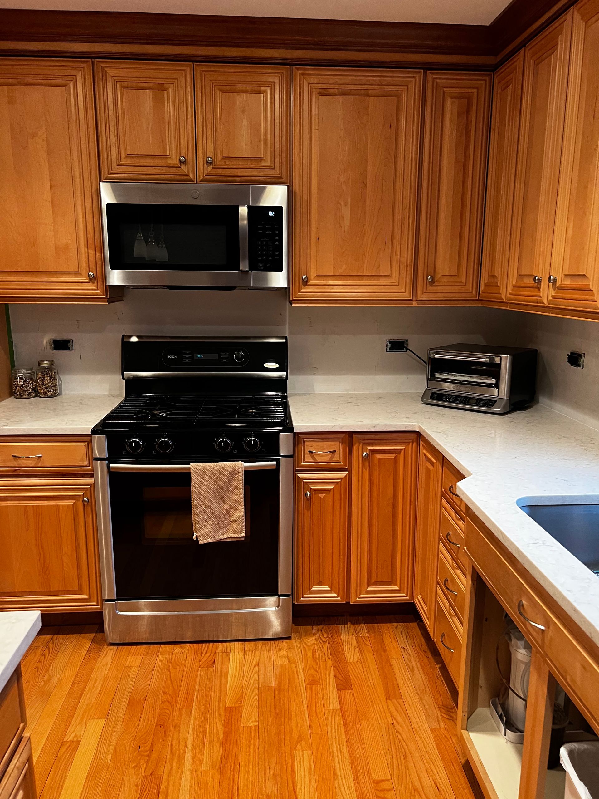Kitchen with wooden cabinets, stainless steel stove and microwave, granite counters, and hardwood floor.