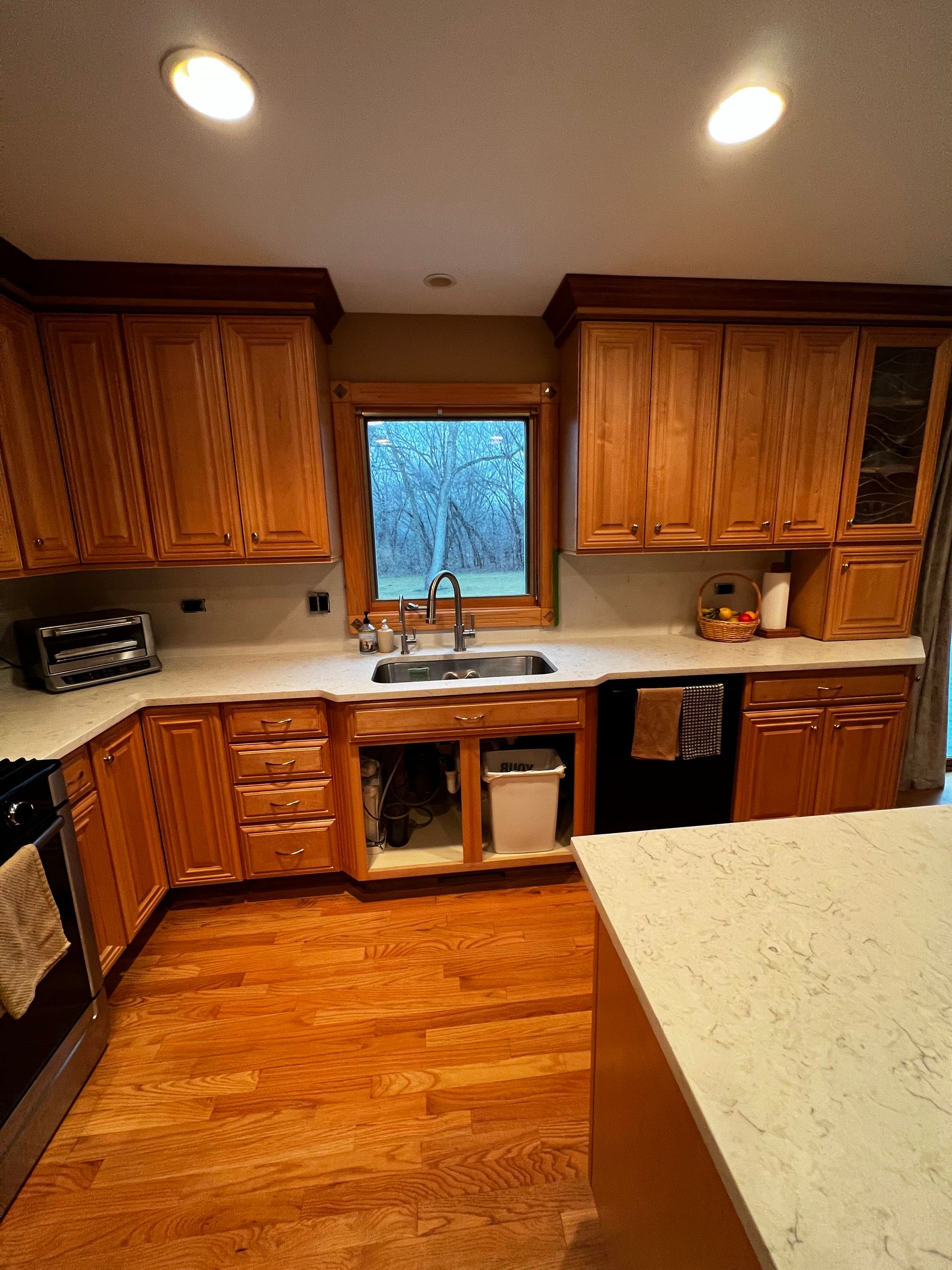 Wooden kitchen with white countertops, center island, and a window over the sink.