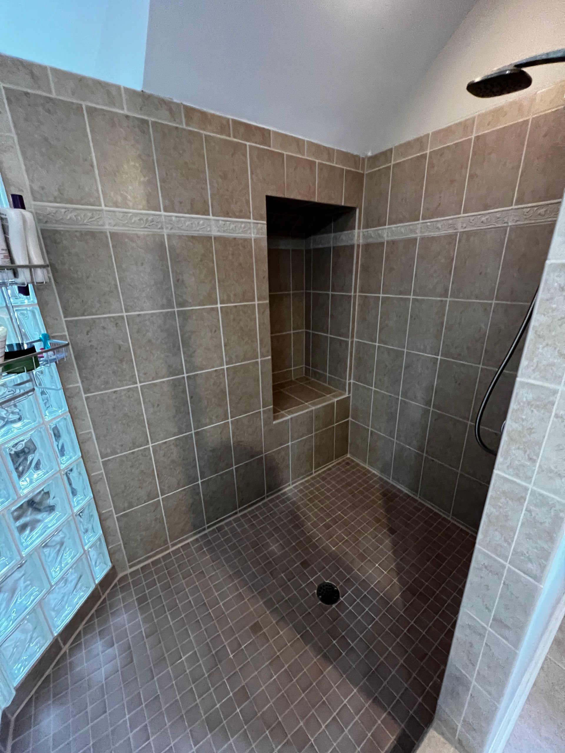 Tiled shower stall with a built-in niche and dark floor drain, viewed from the doorway.