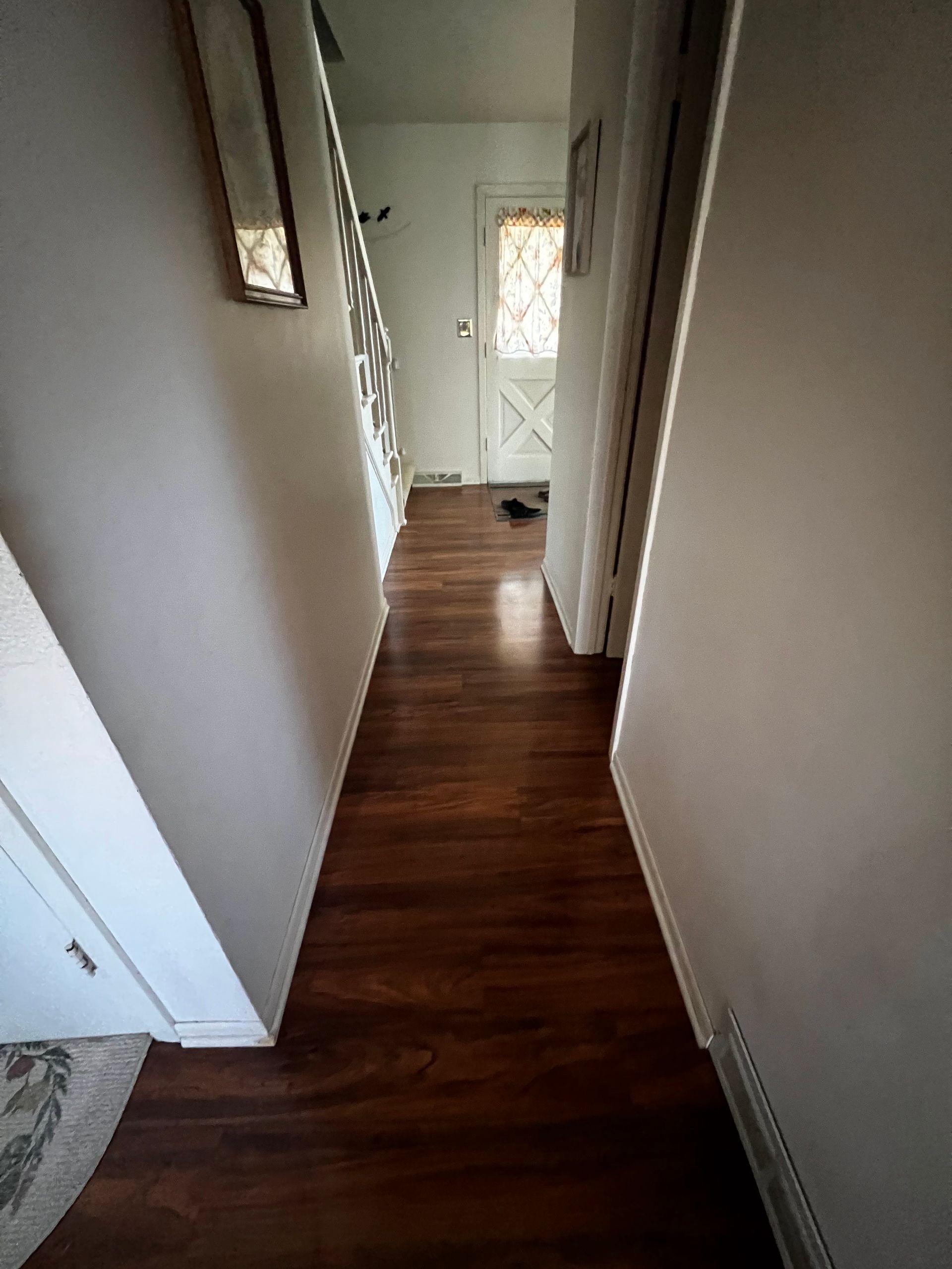 Narrow hallway with dark wood floor, white walls, and a front door at the end.