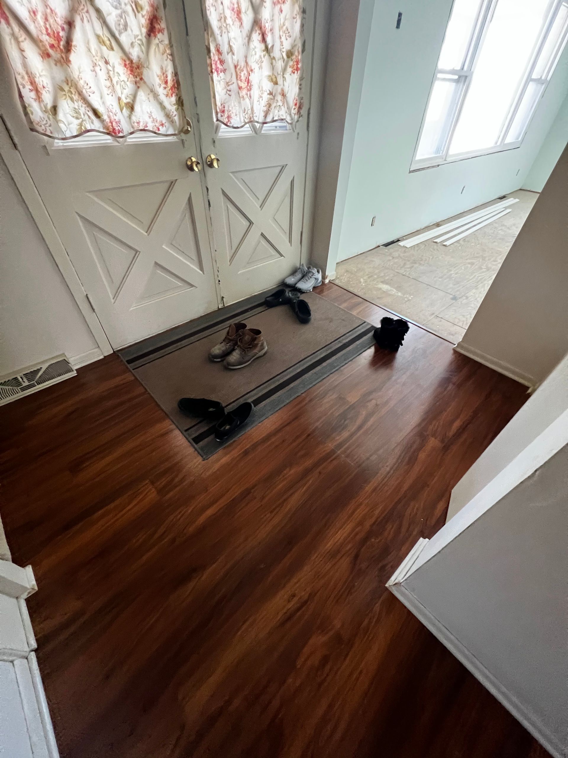 Entryway with a doormat, shoes, and a white front door with patterned curtains