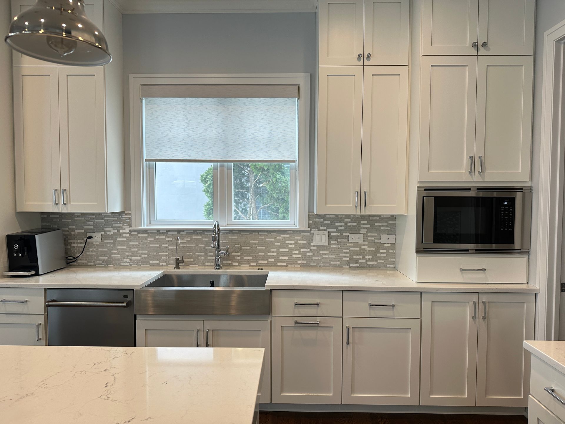 Modern white kitchen with stainless steel appliances, mosaic backsplash, and a window above the sink