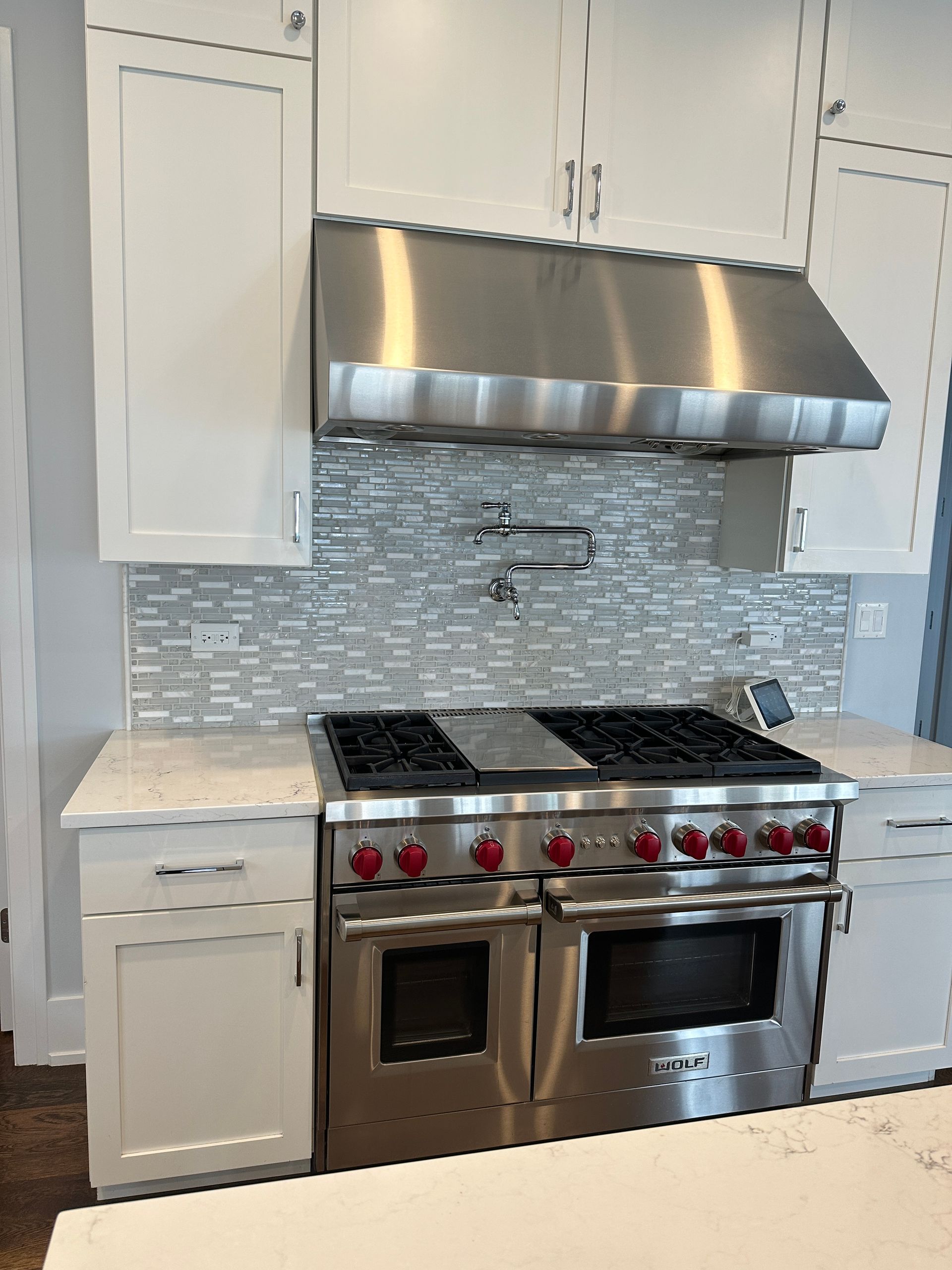 Modern kitchen with white cabinets, stainless steel range hood and oven, and mosaic tile backsplash