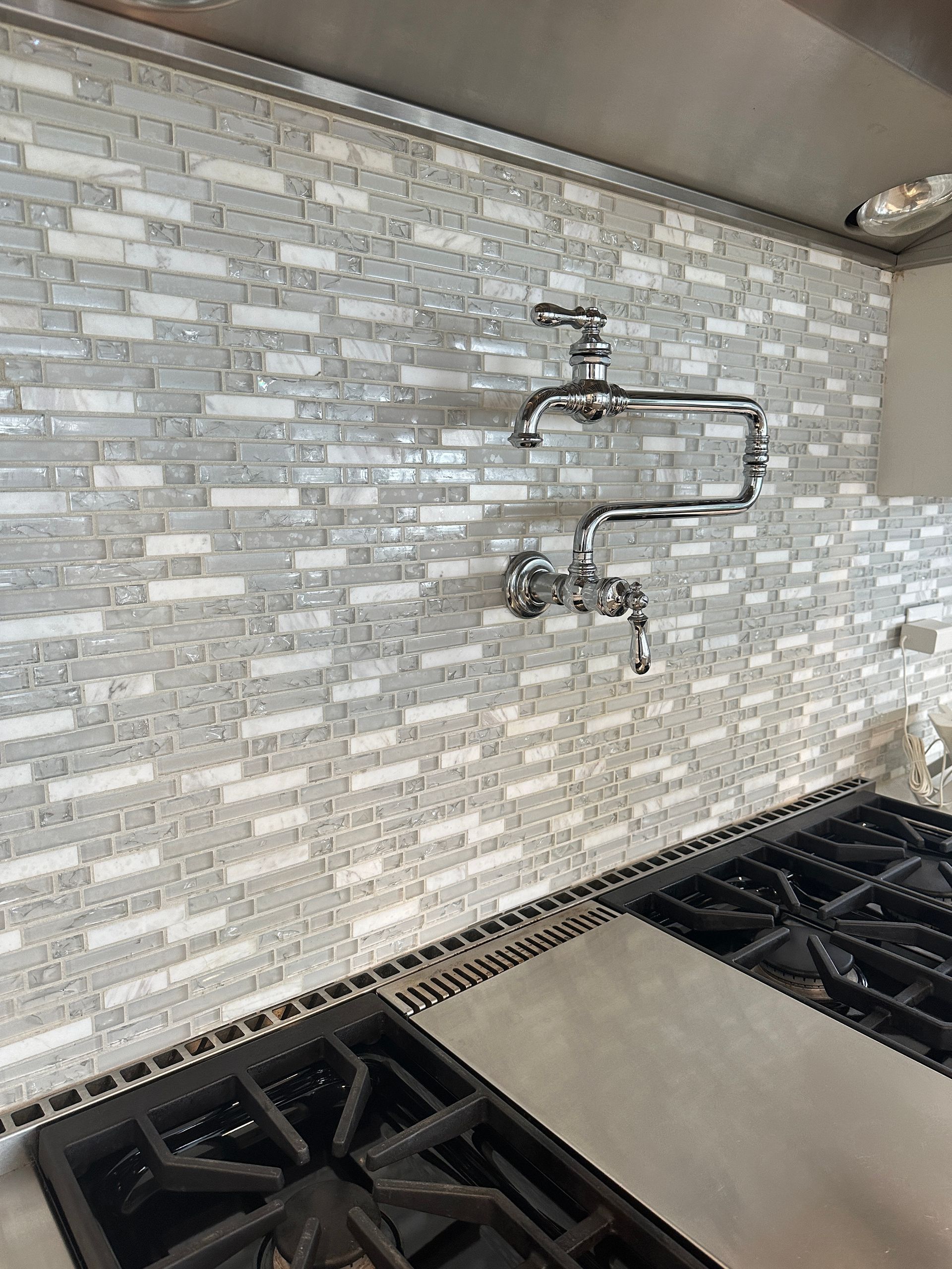 Kitchen backsplash with mosaic tile and wall-mounted pot filler above a gas stove.