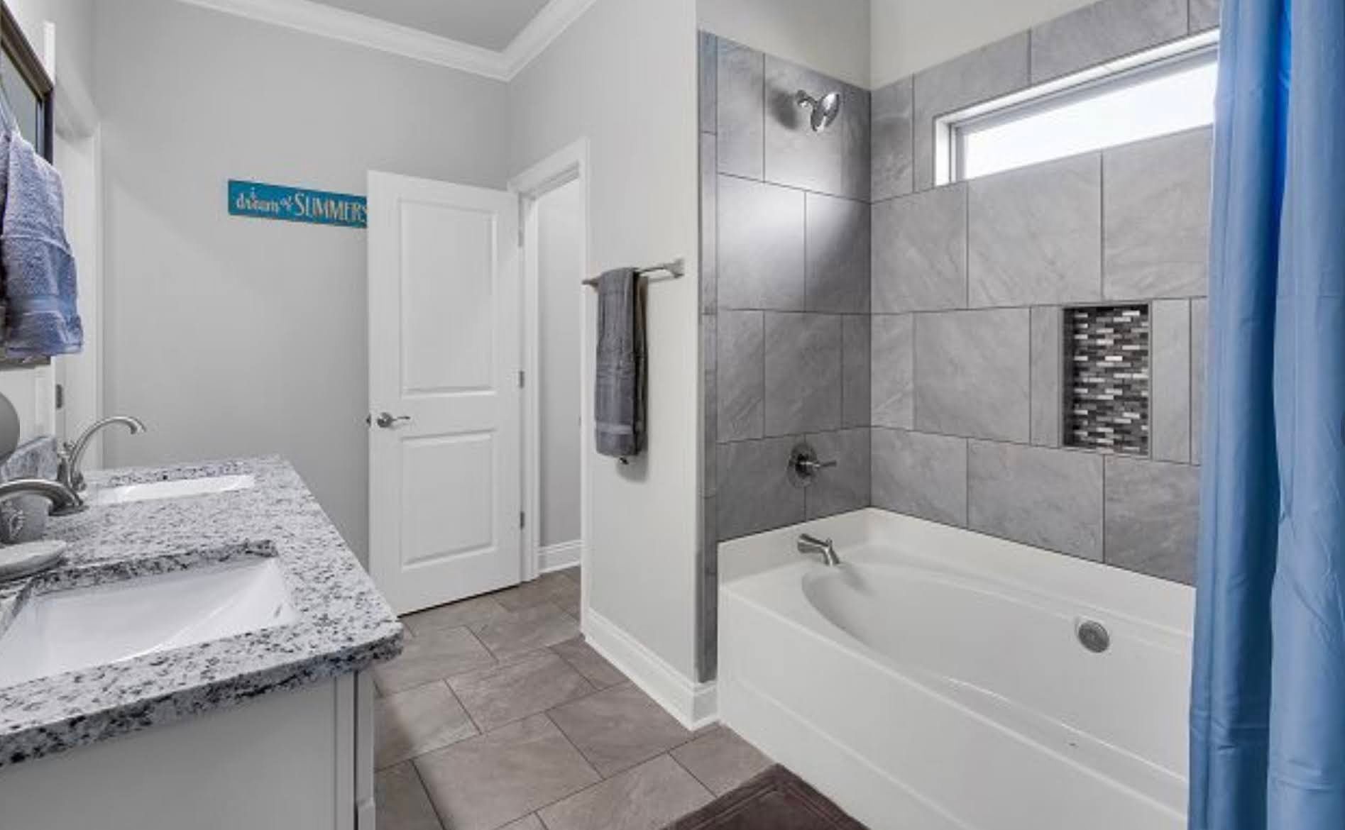 Modern gray bathroom with white vanity and bathtub, tiled shower walls, and blue curtain
