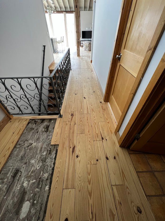 Narrow upstairs hallway with light wood flooring, white walls, and a staircase with decorative iron railing.