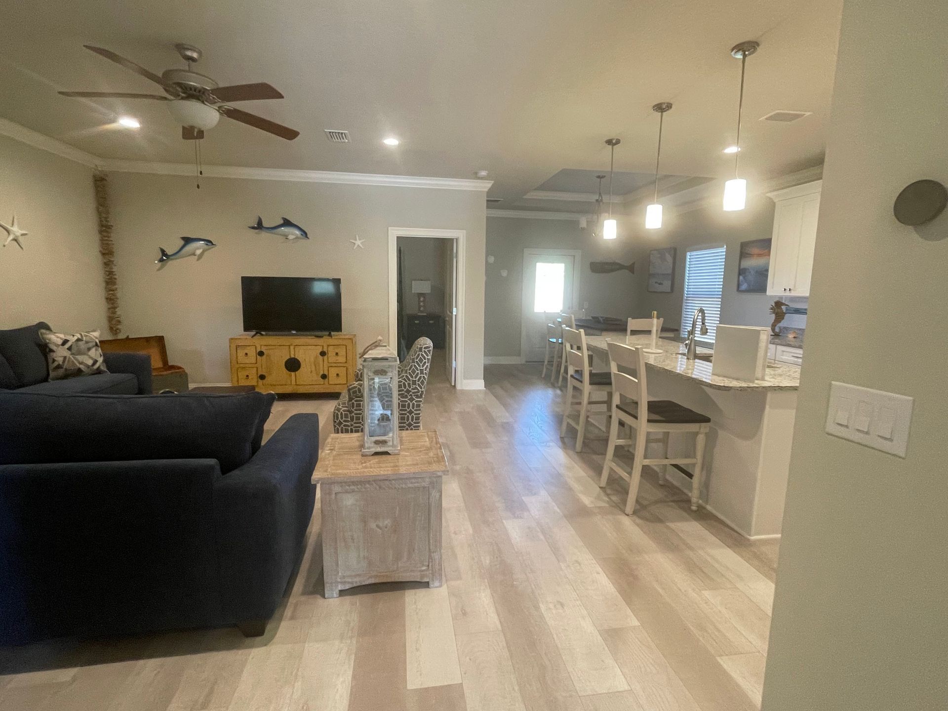 Open-concept living room and kitchen with beige floors, dark sofa, TV, and dining island under pendant lights