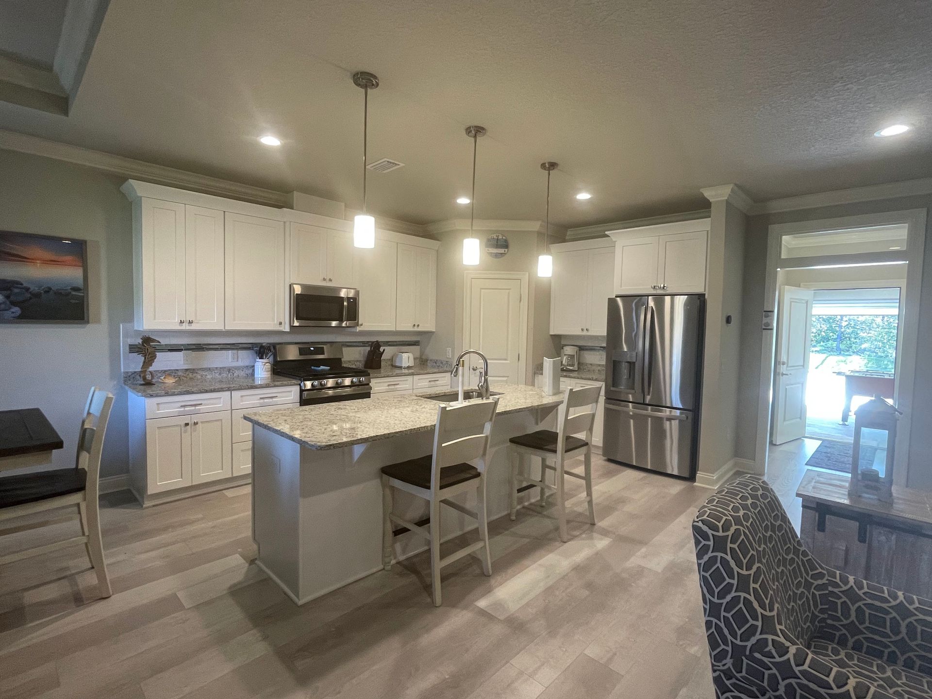 Modern white kitchen with island, stainless steel appliances, pendant lights, and a dining table by a bright window.