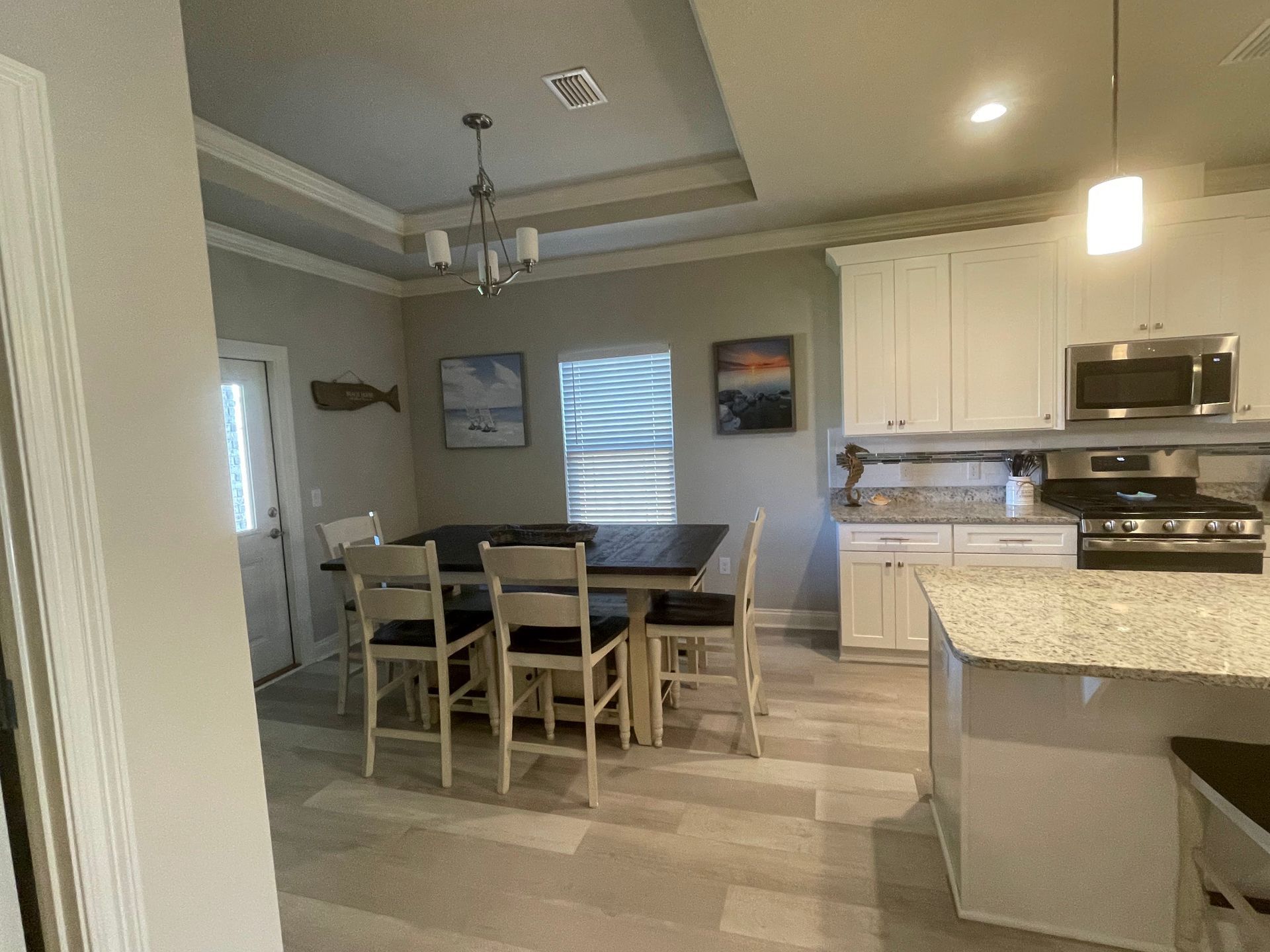 Kitchen and dining area with white cabinets, granite island, and a wooden table under pendant lights.