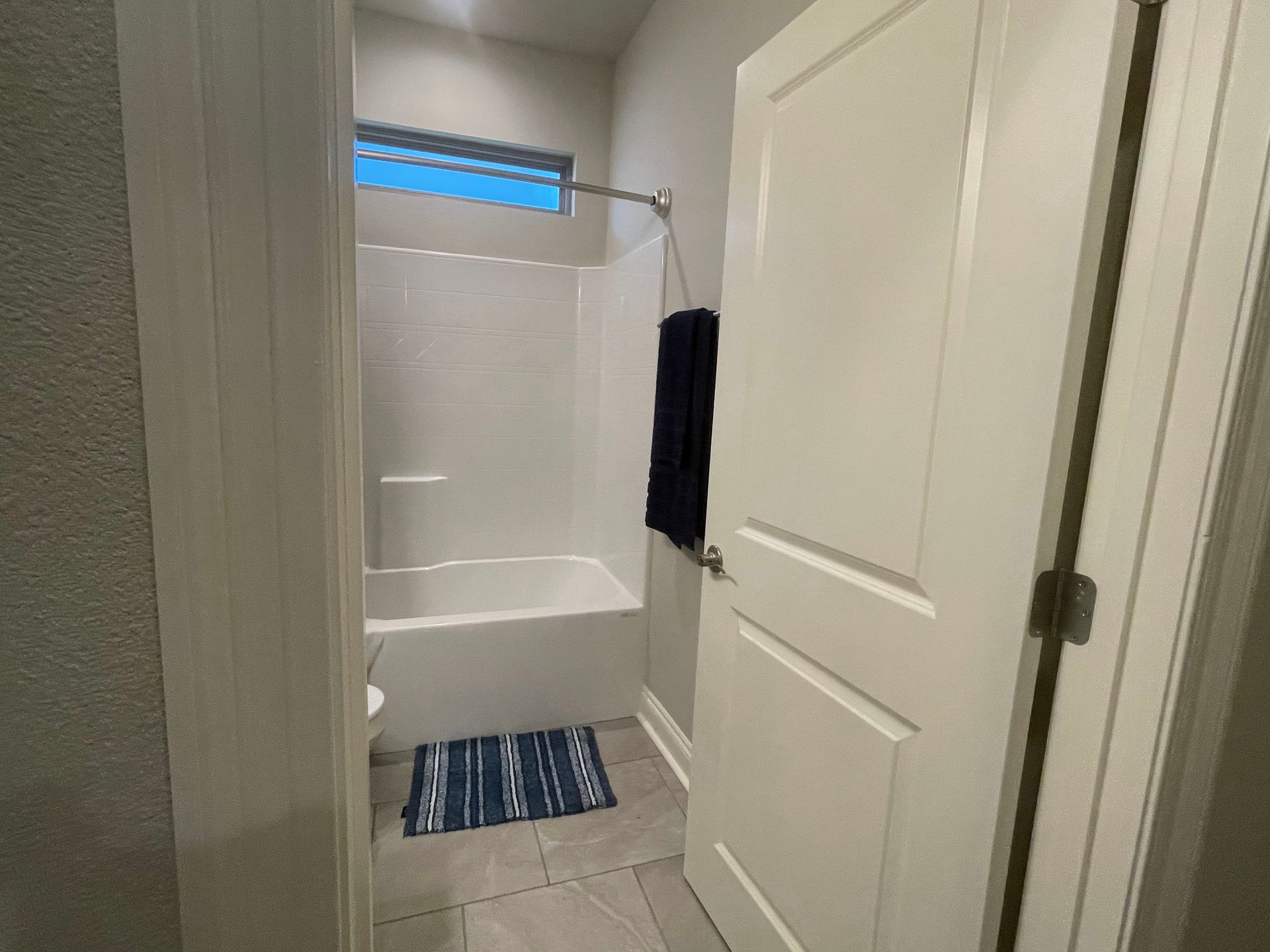 Bathroom doorway with shower, blue rug, and partially open white door