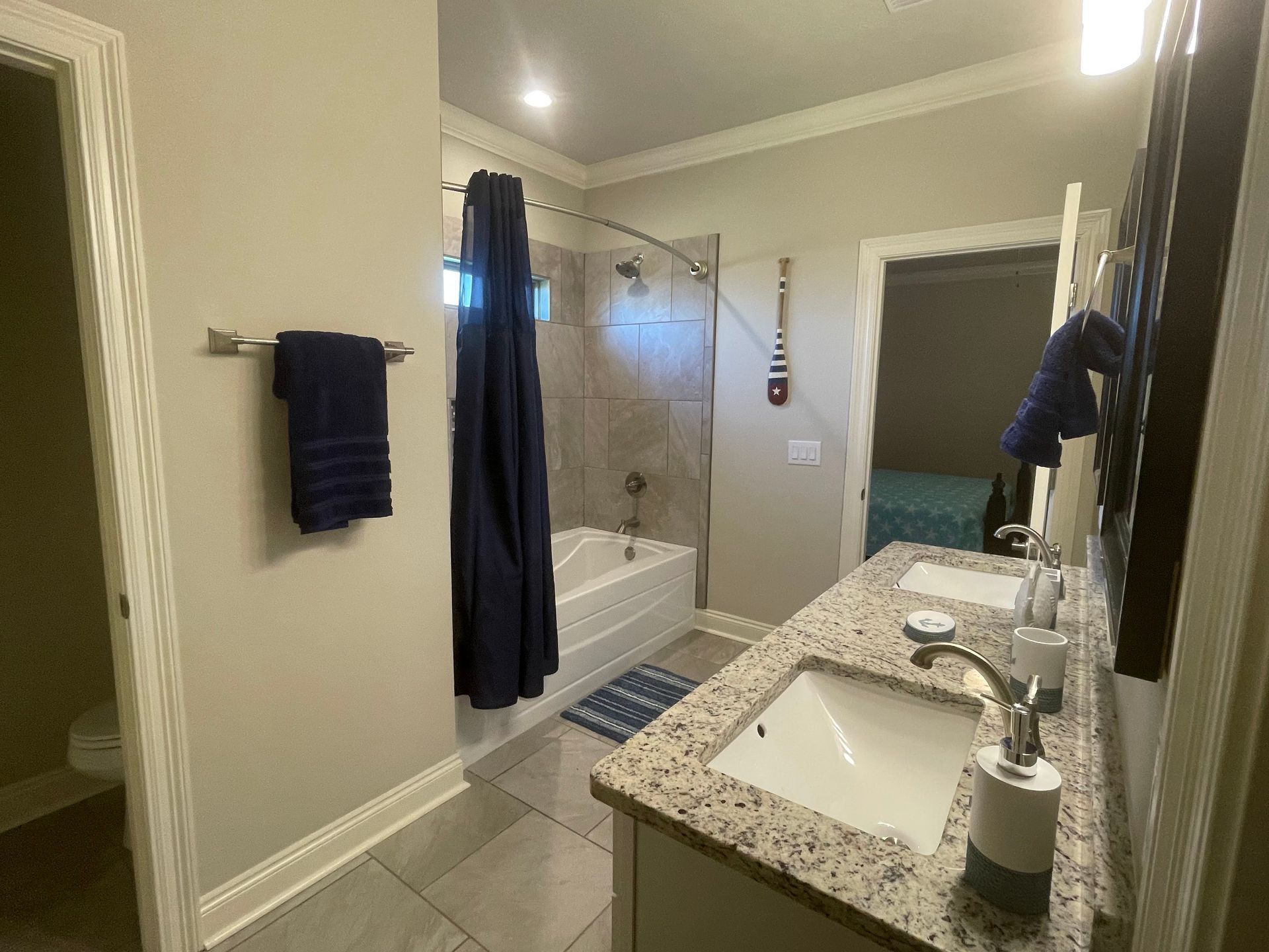 Modern bathroom with granite vanity, shower curtain, tub, towel racks, and blue accents