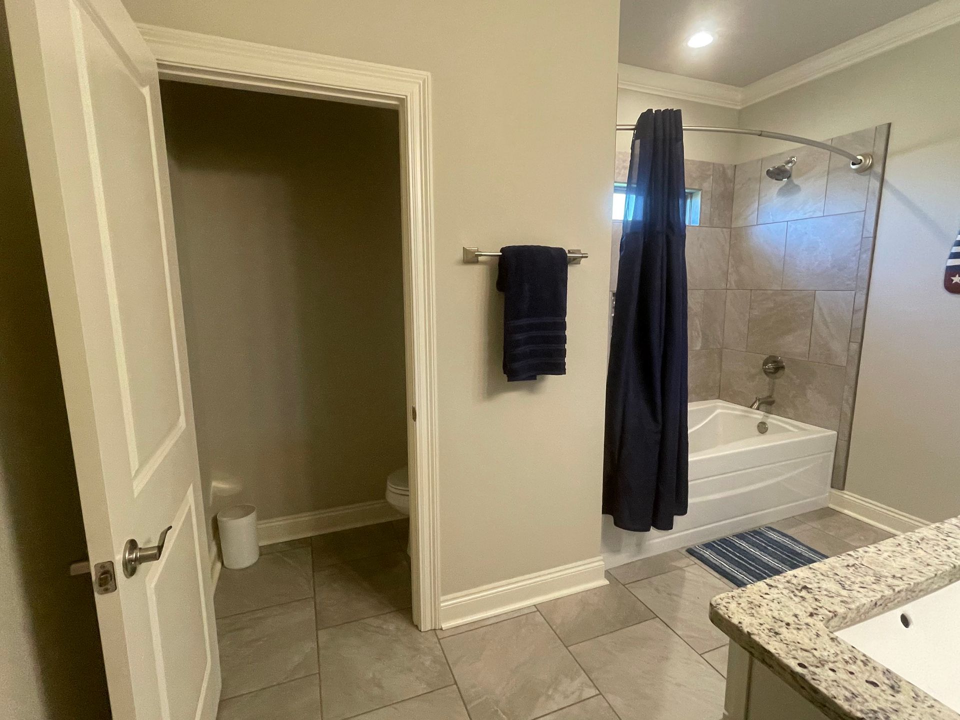Bathroom with beige walls, granite vanity, tub-shower enclosure, and an open doorway to a toilet closet