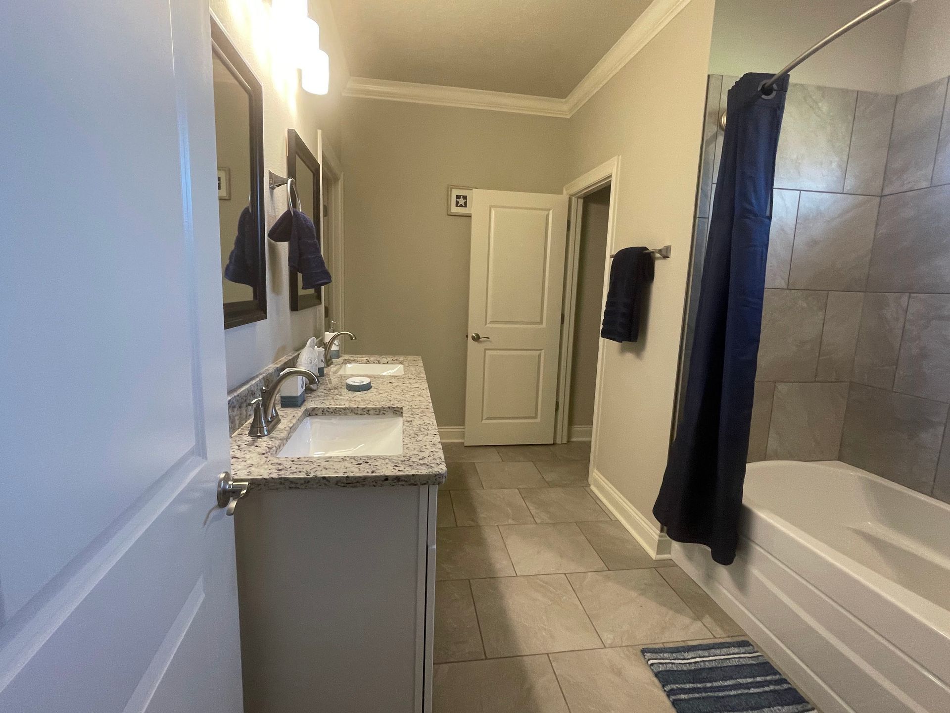 Bathroom with gray tile, white vanity, bathtub, and dark towels hanging on the wall.