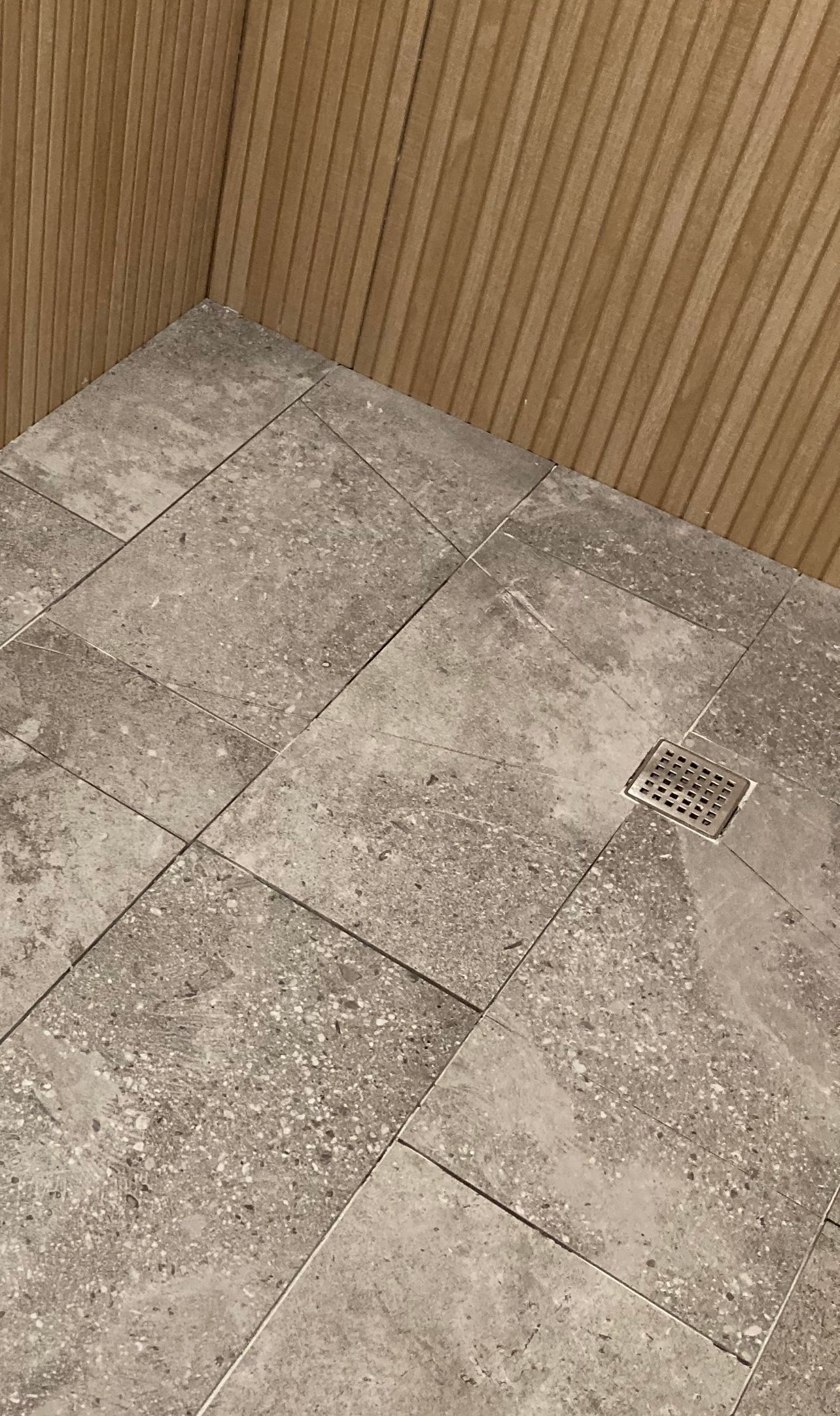 Corner of a tiled shower floor with a small drain and wood-paneled walls