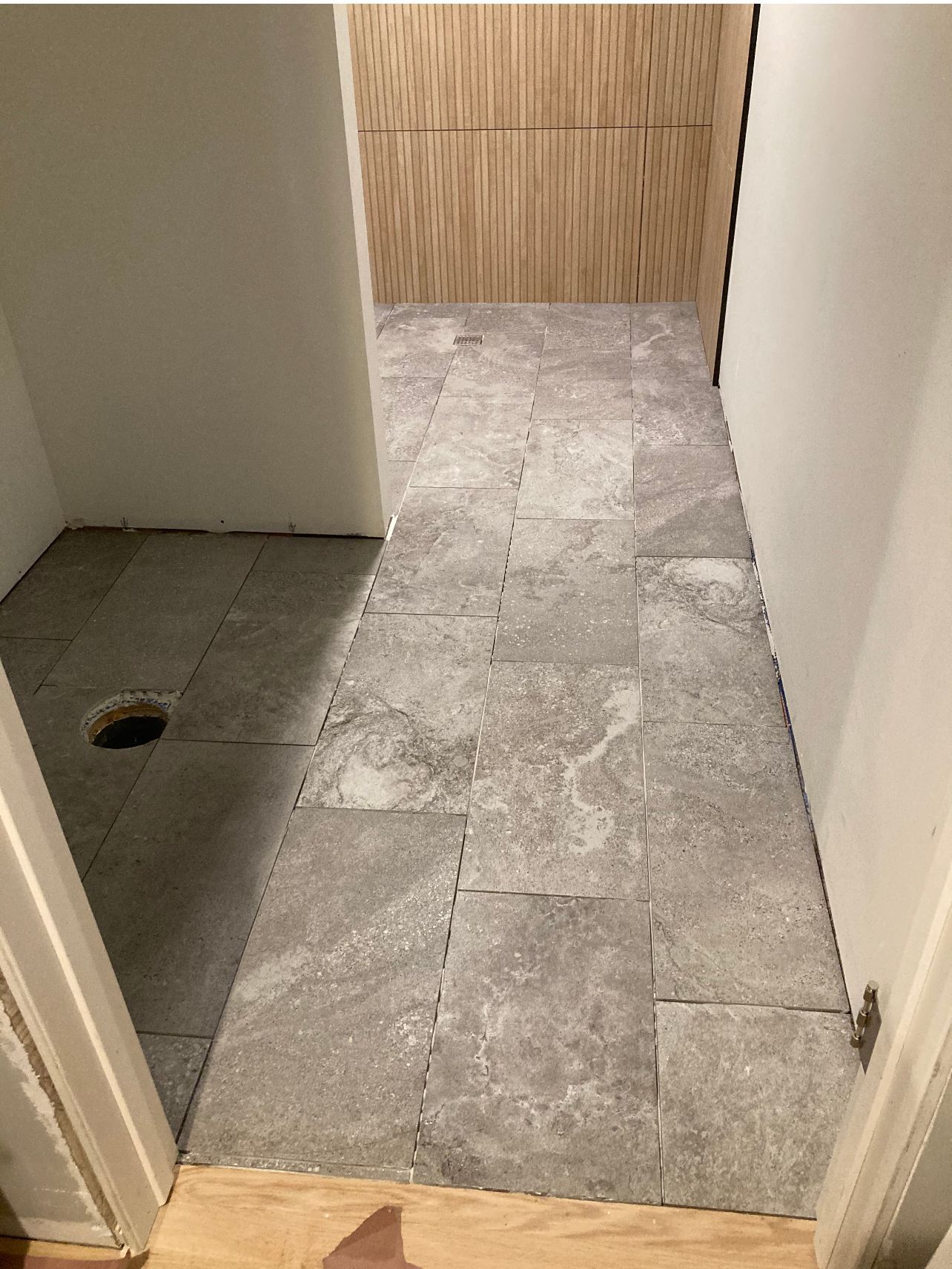 Small tiled bathroom under construction with a floor drain and unfinished shower area.