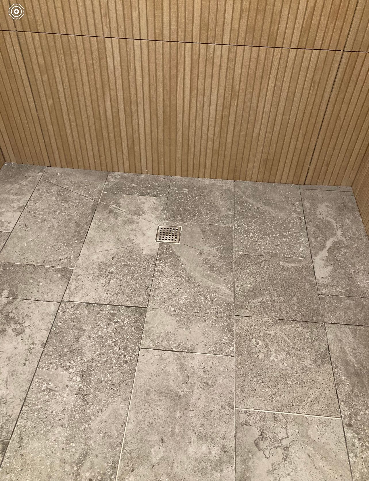 Stone-tiled floor with a small drain and a bamboo or wood-paneled wall behind it