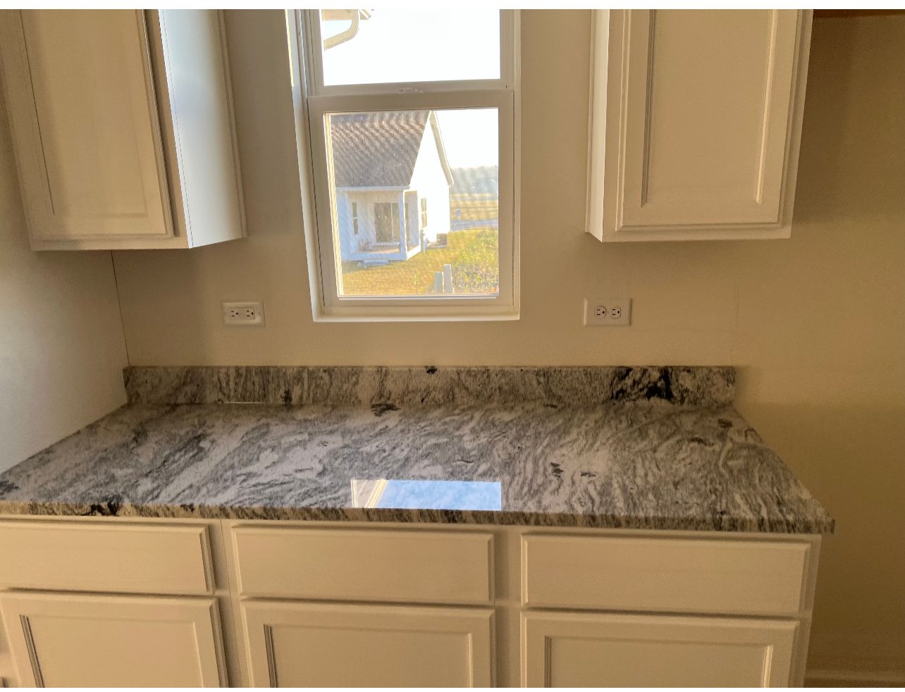 Kitchen countertop with beige cabinets, granite surface, and a window above the sink area