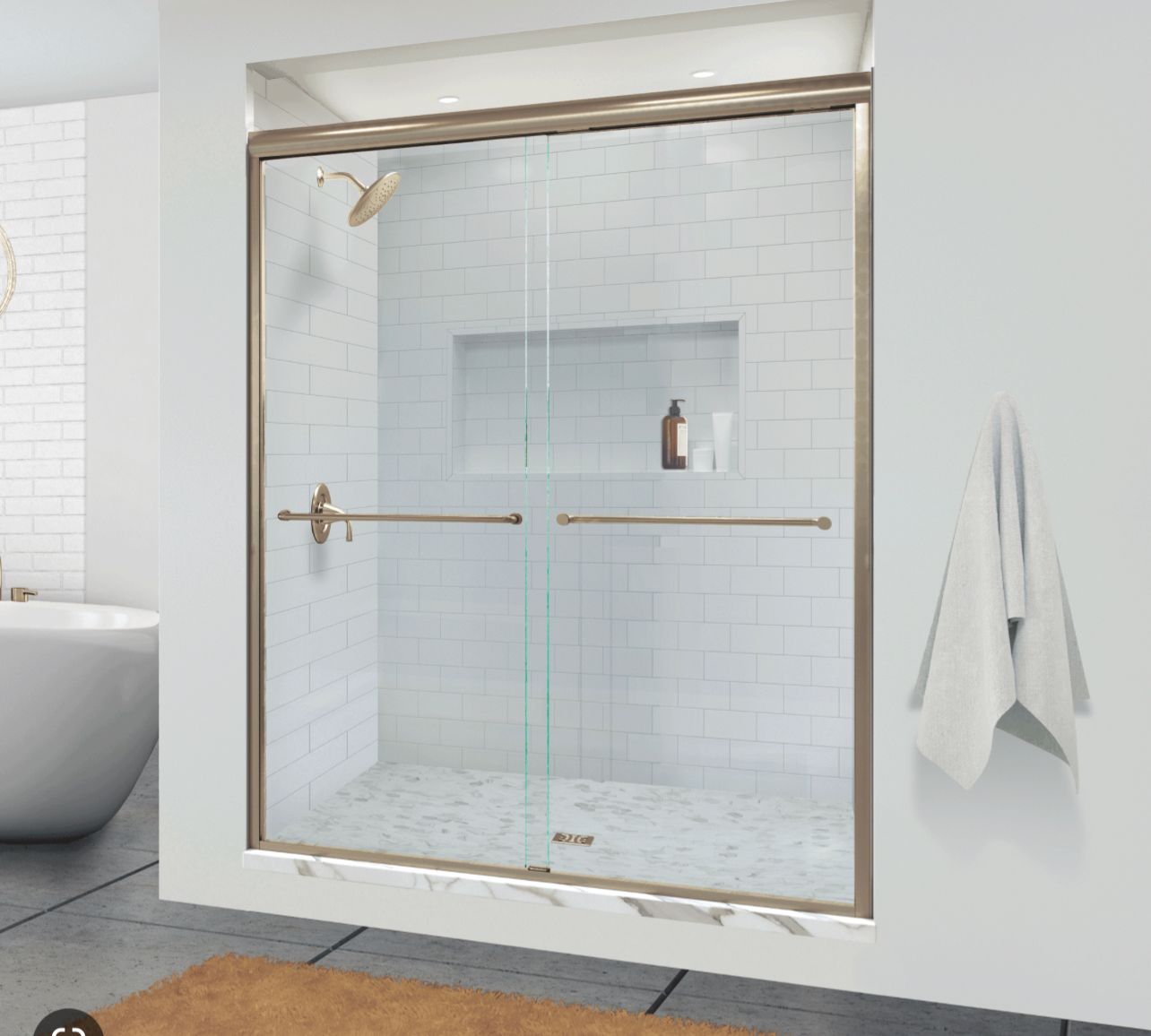 Glass shower enclosure with gold trim in a white-tiled bathroom, with towels hanging on the wall.