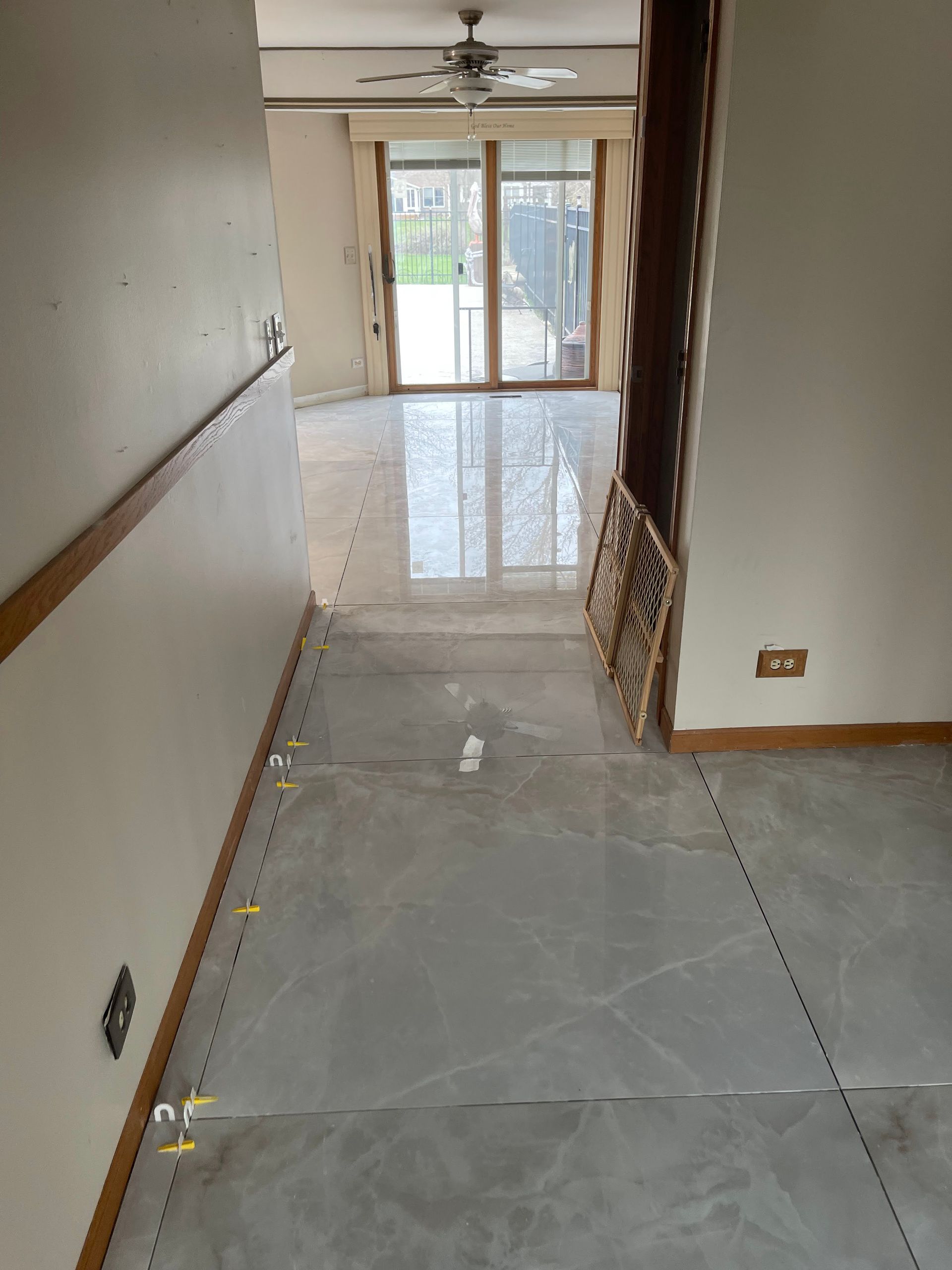 Empty hallway with glossy tile floor, ceiling fan, and sliding glass doors at the far end