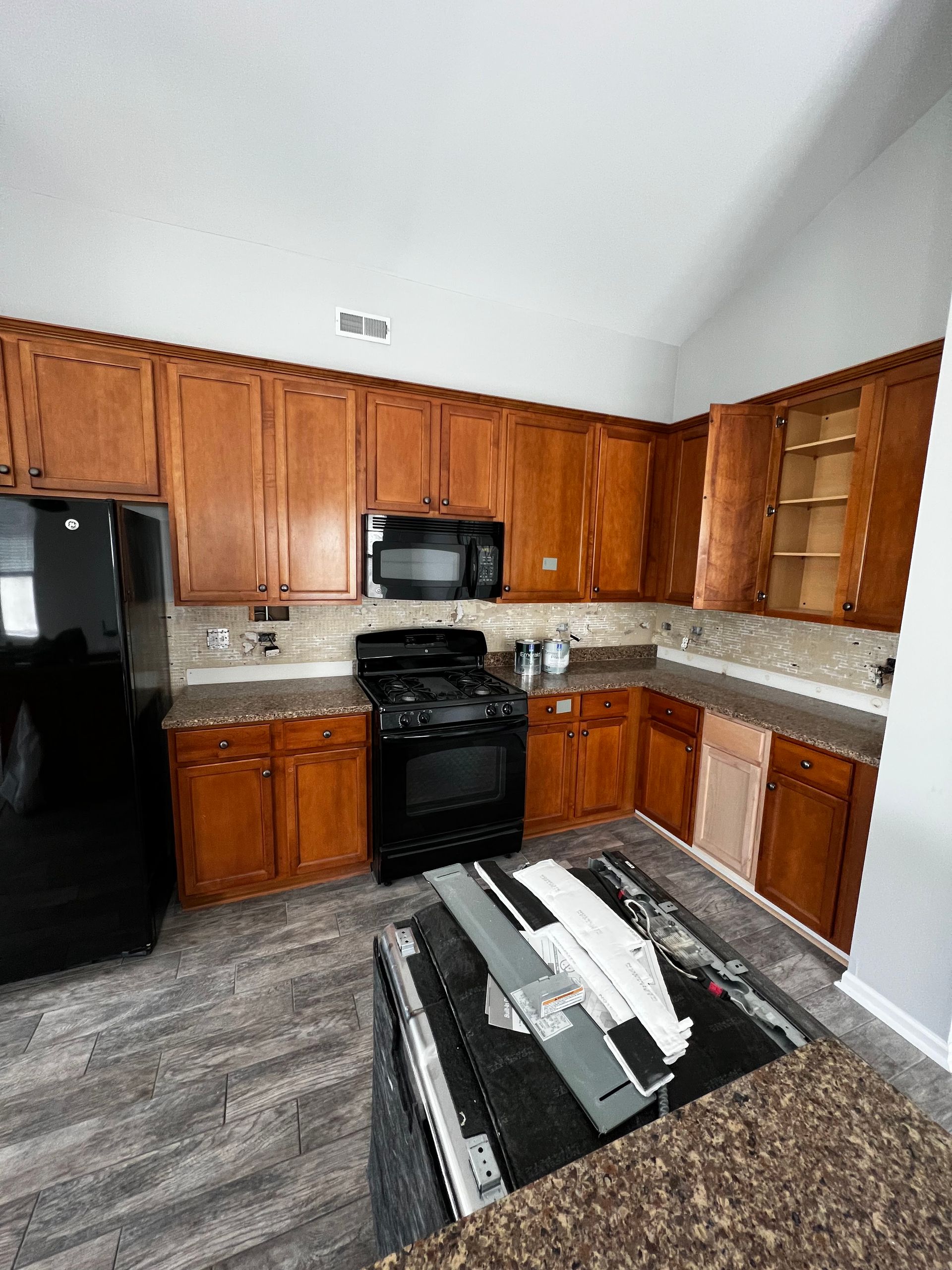 Modern kitchen with wooden cabinets, black appliances, granite counters, and gray wood-look flooring.