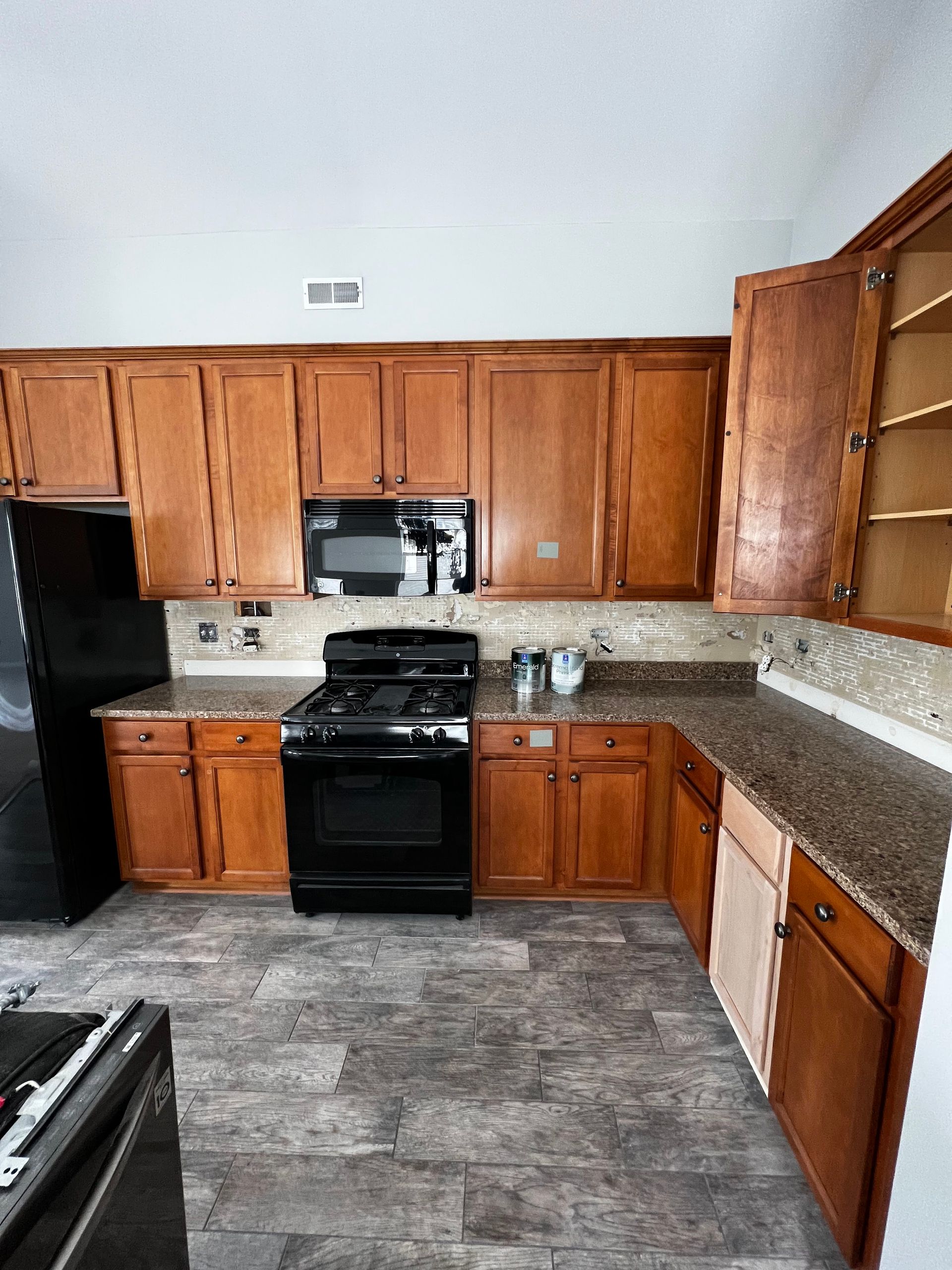Empty kitchen with wood cabinets, black stove, granite counters, and gray tile floor.