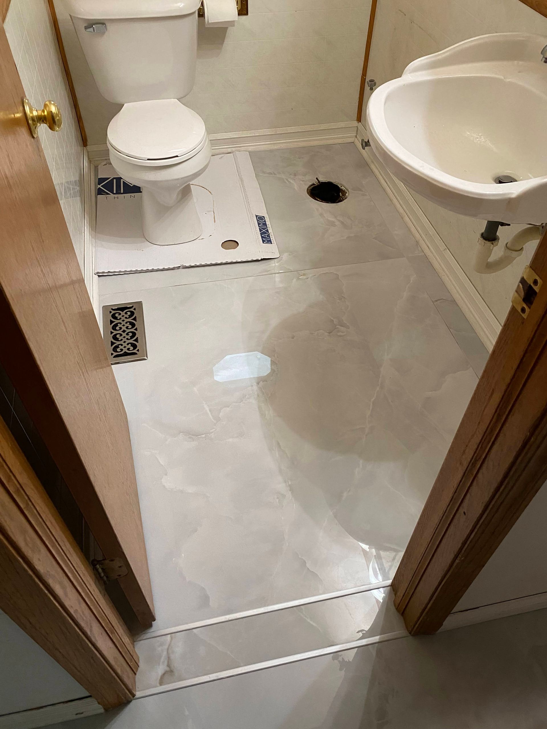 Small bathroom with toilet, sink, and wet floor around a drain near the doorway.