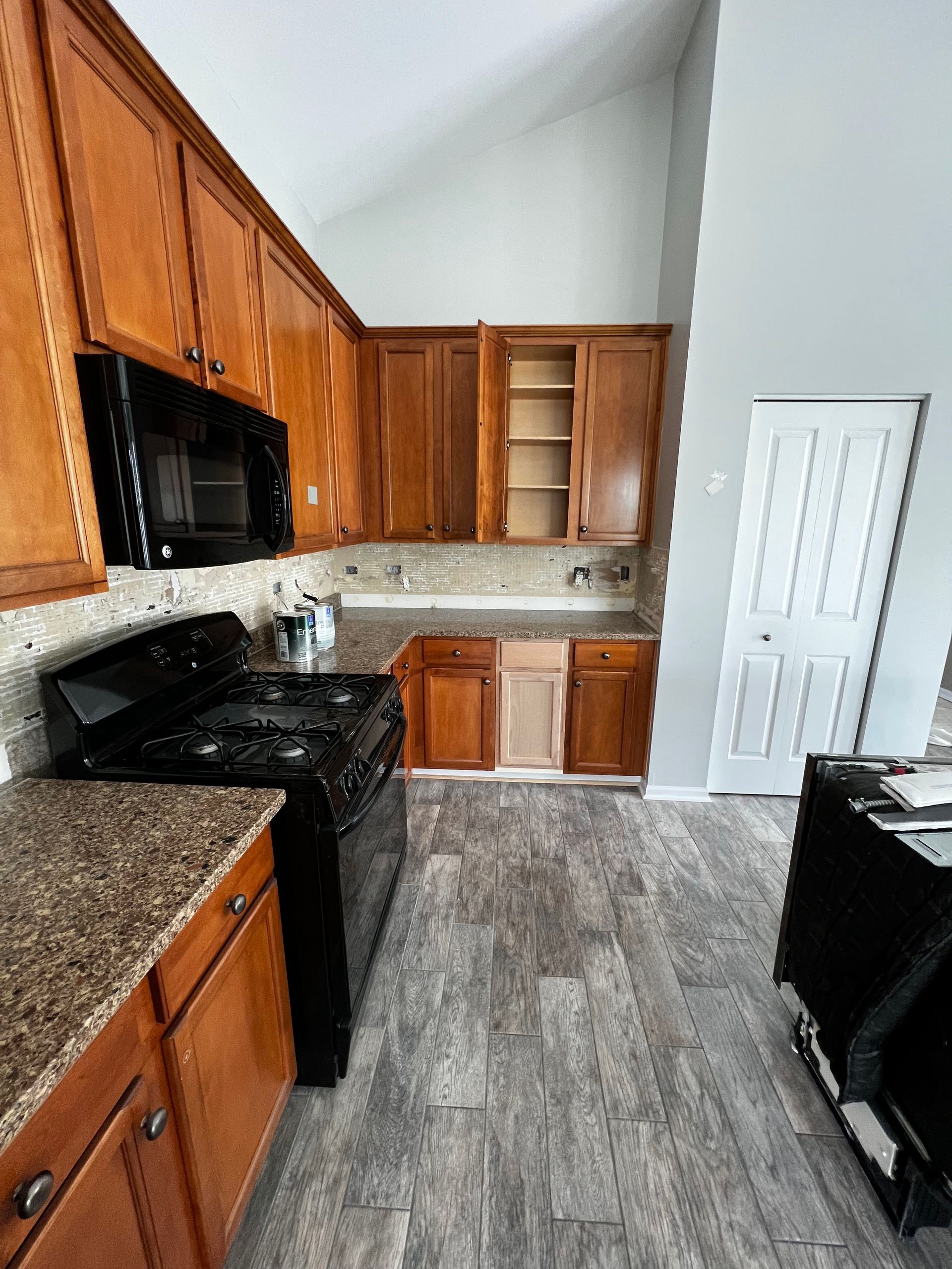 Compact kitchen with wood cabinets, black appliances, granite counters, and gray wood-look flooring.