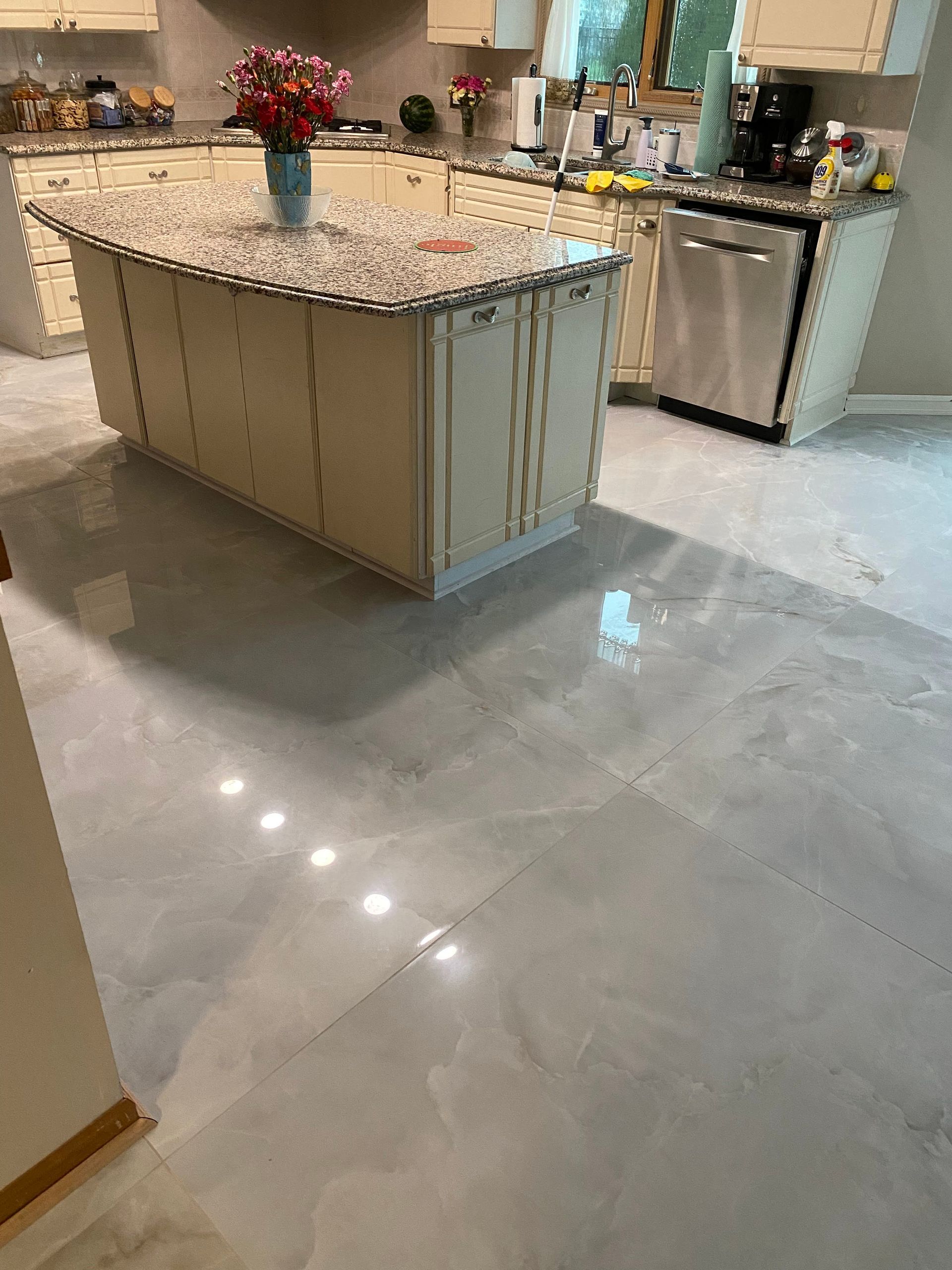 Modern kitchen with a large granite island, polished gray floor, and vase of flowers on the counter