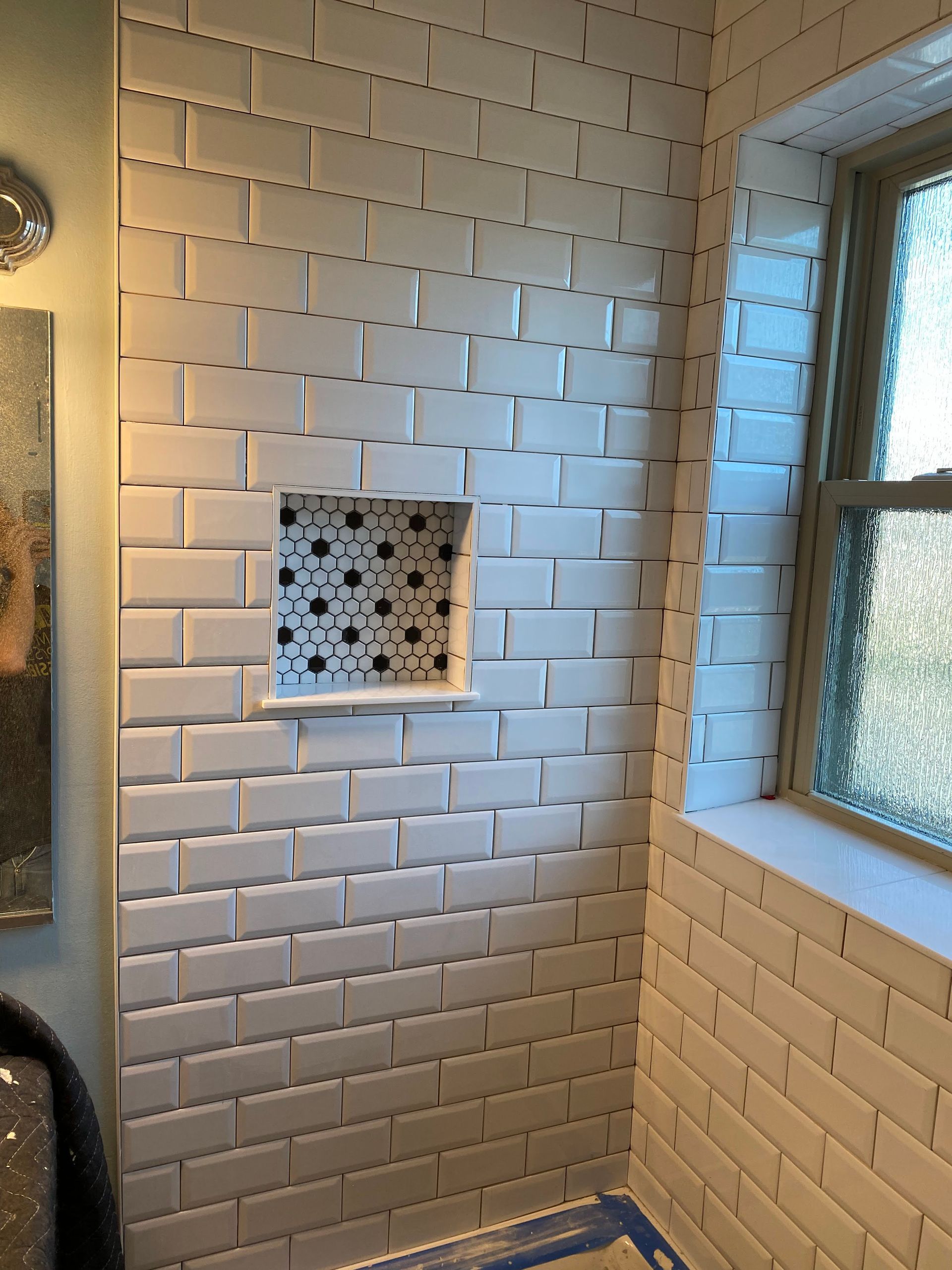 White tiled shower wall with a built-in niche and a frosted window on the right.