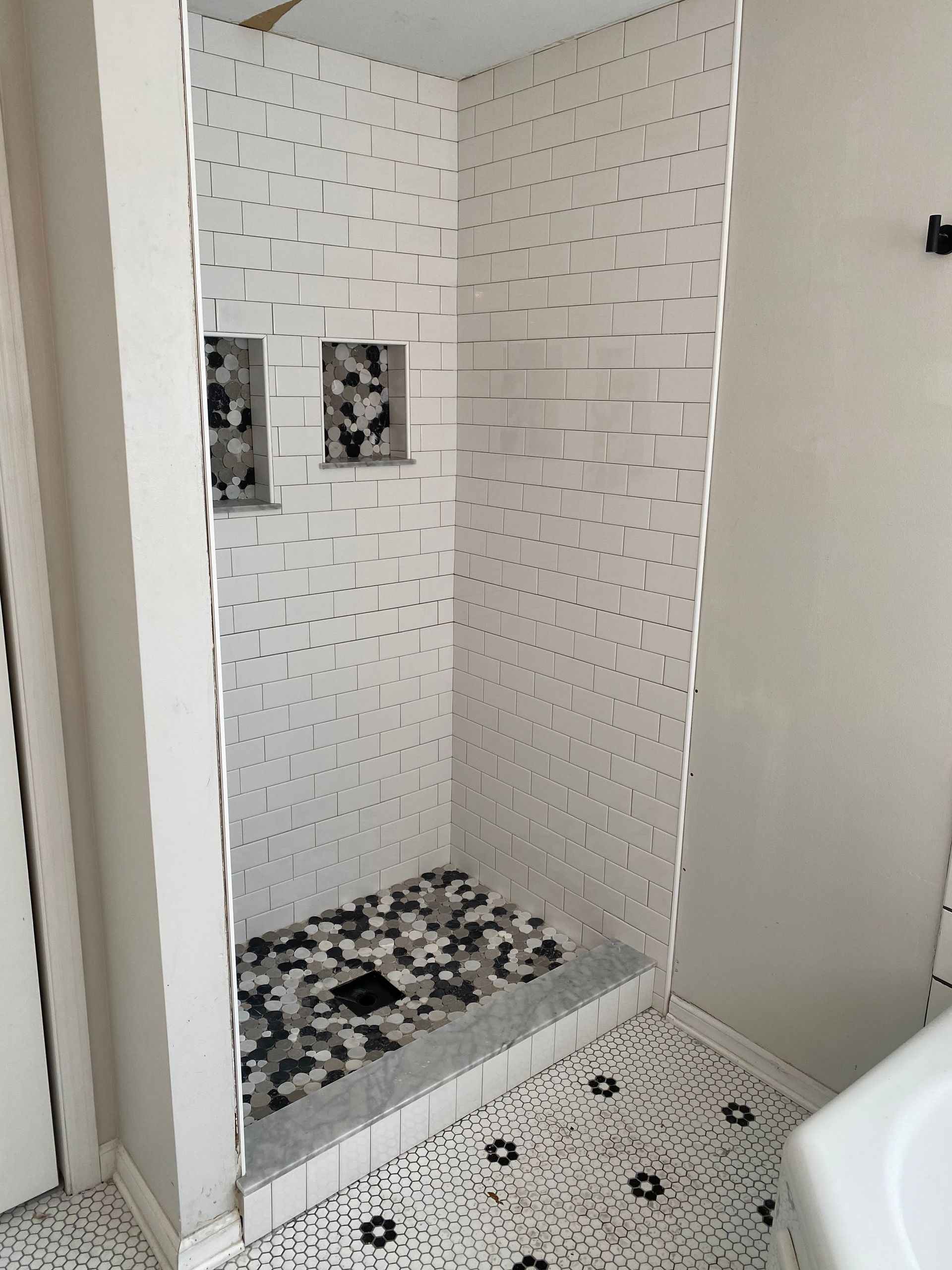 Empty tiled shower stall with white walls and black-and-white mosaic floor trim.