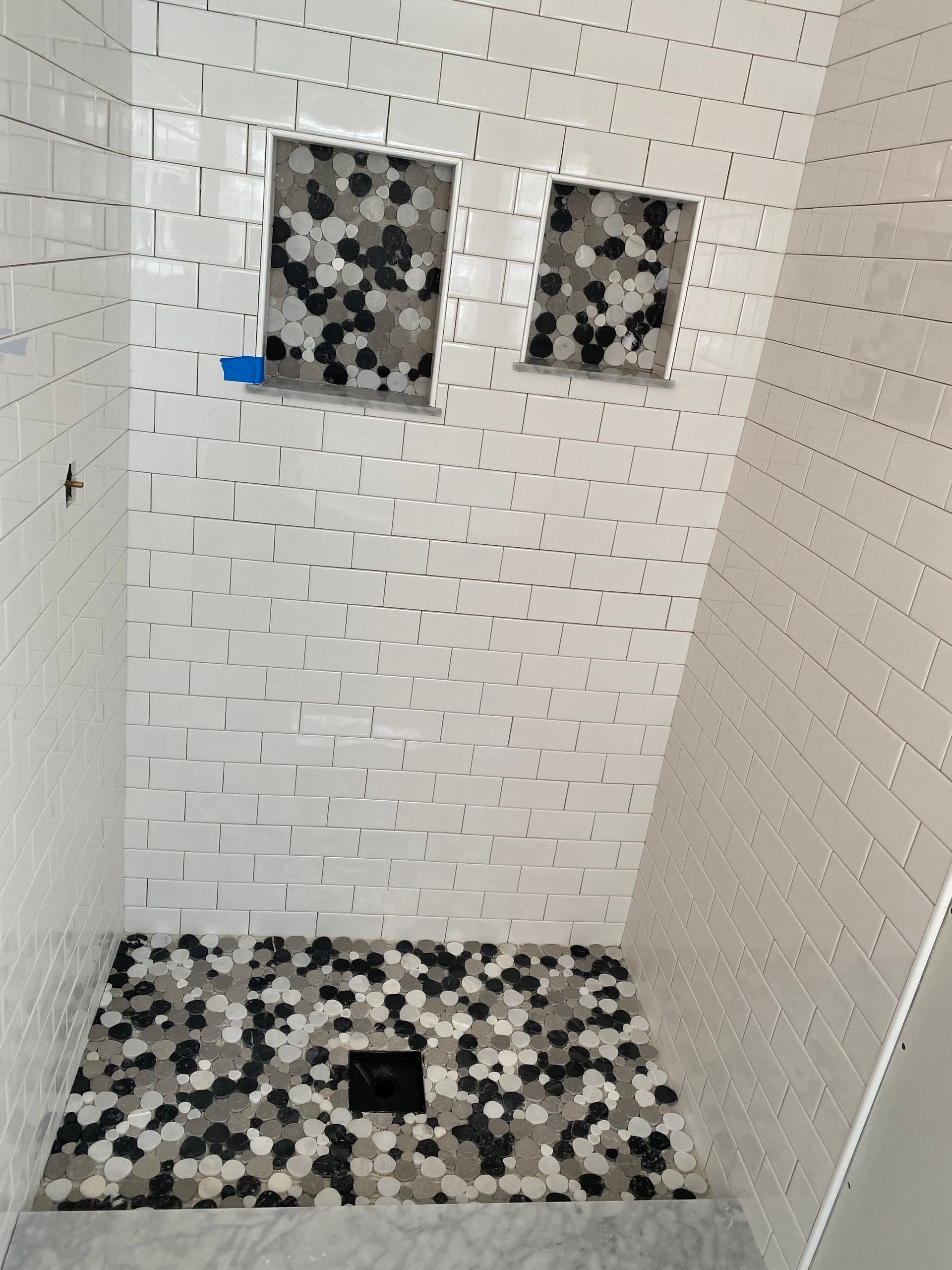 White tiled shower with black-and-white mosaic accent niches and matching floor trim.
