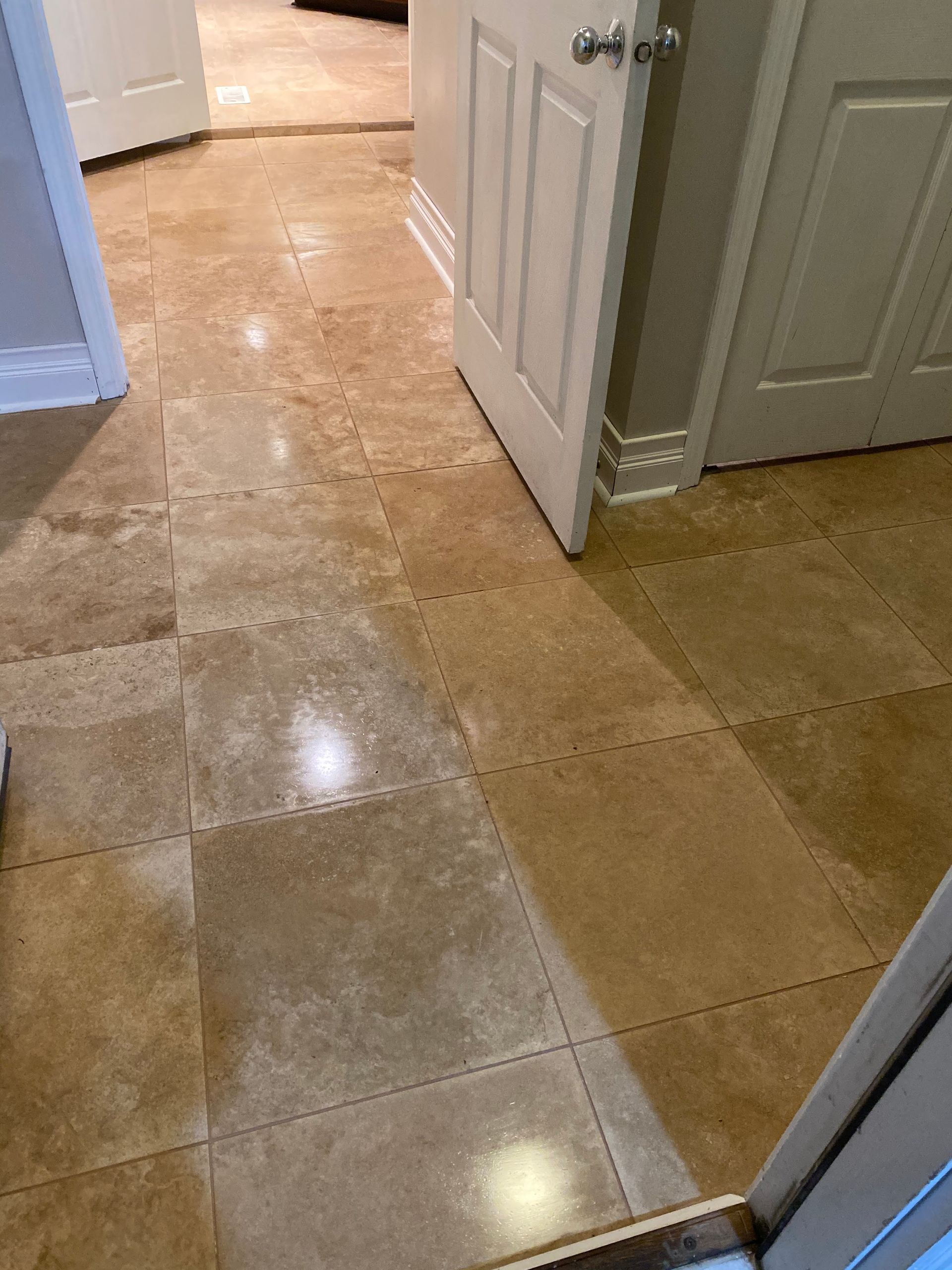 Hallway with glossy tan tile floor and open white doors leading into adjacent rooms.