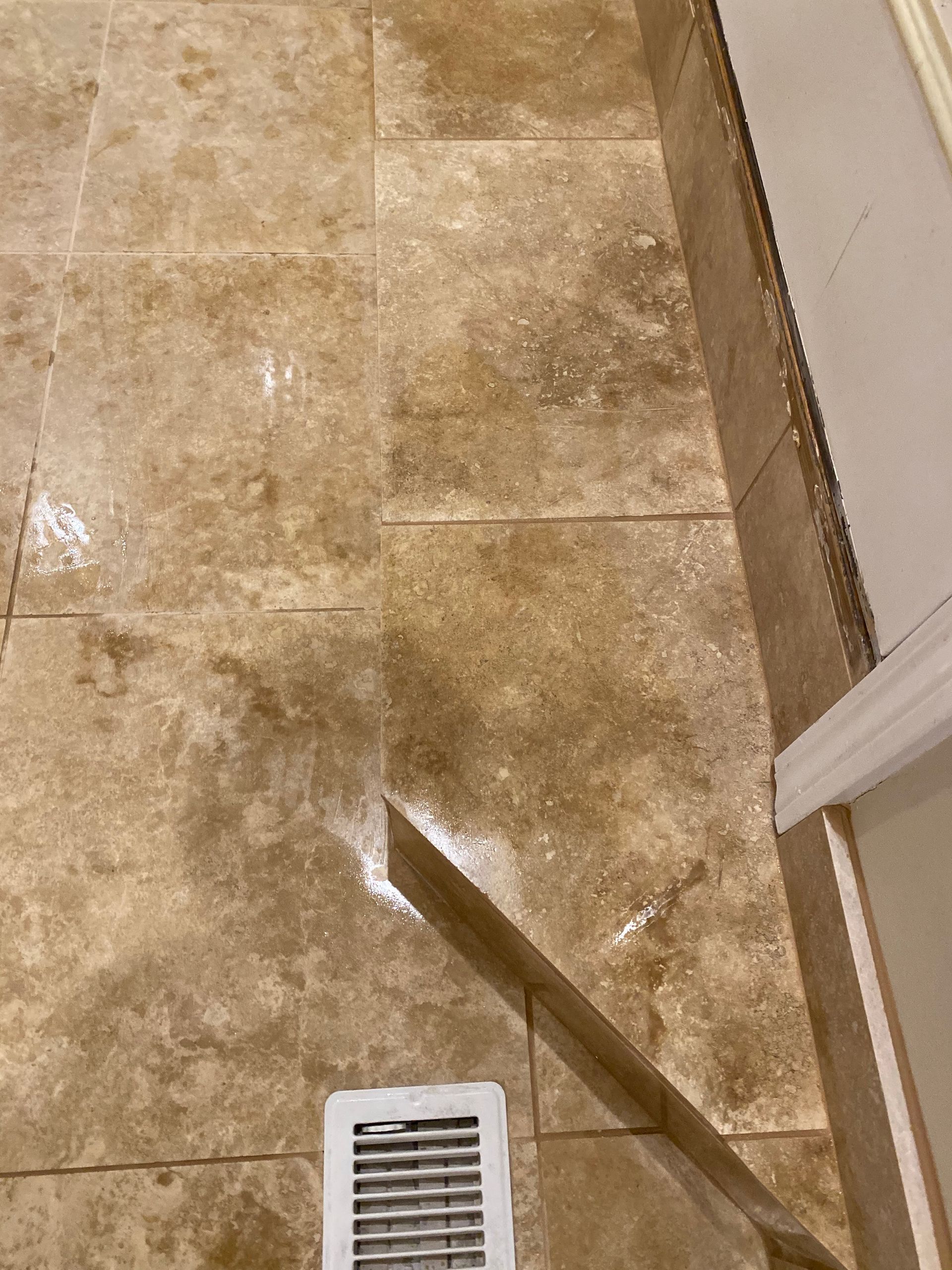 Tan tiled floor with a floor vent and a diagonal strip of light near a wall opening