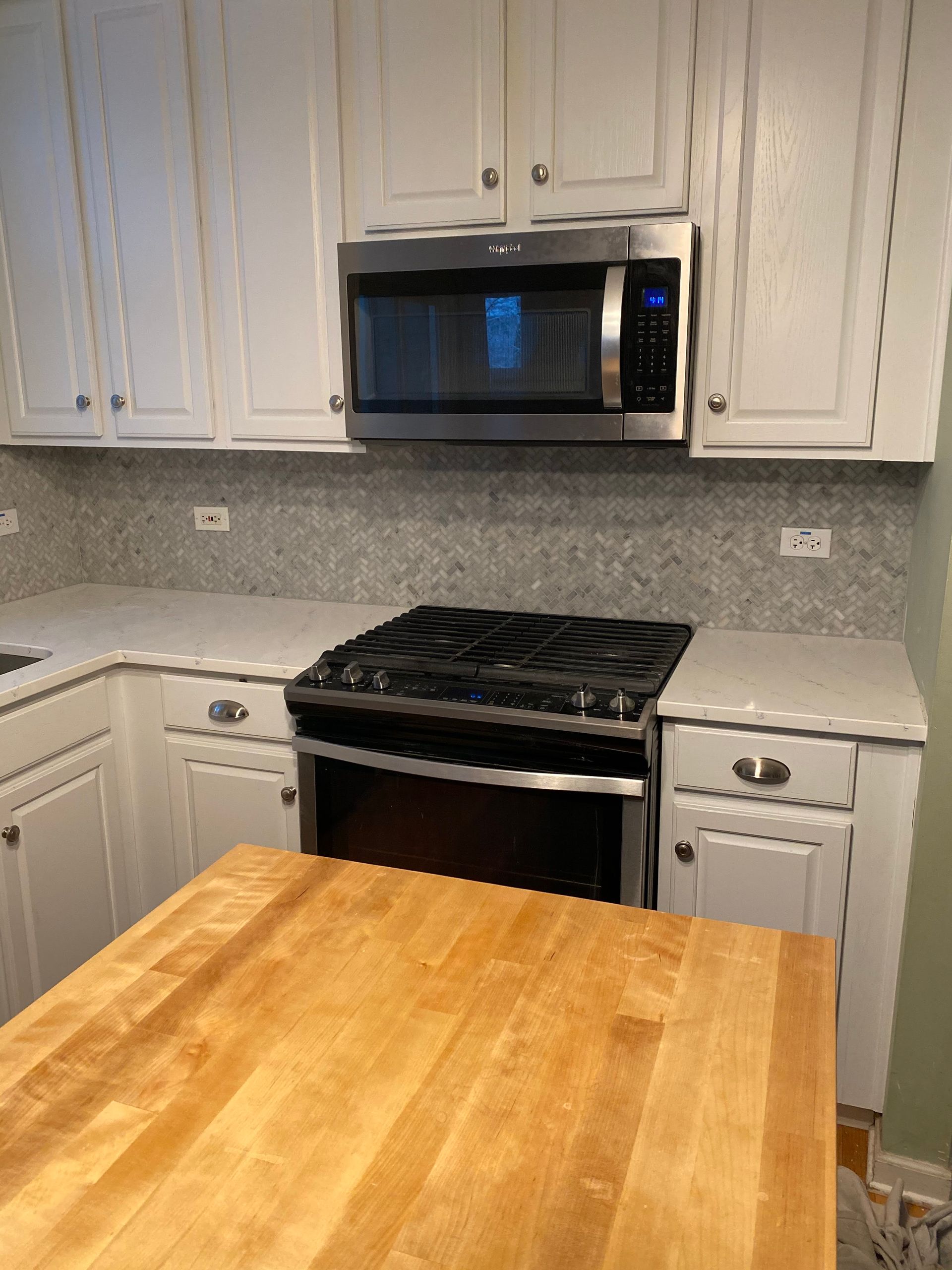 Kitchen with white cabinets, stainless steel microwave, black stove, and a wooden island countertop.