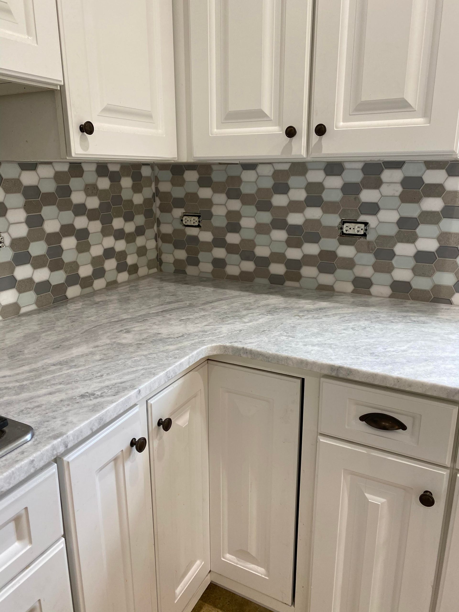 White kitchen corner with granite countertop, gray tile backsplash, and upper and lower cabinets