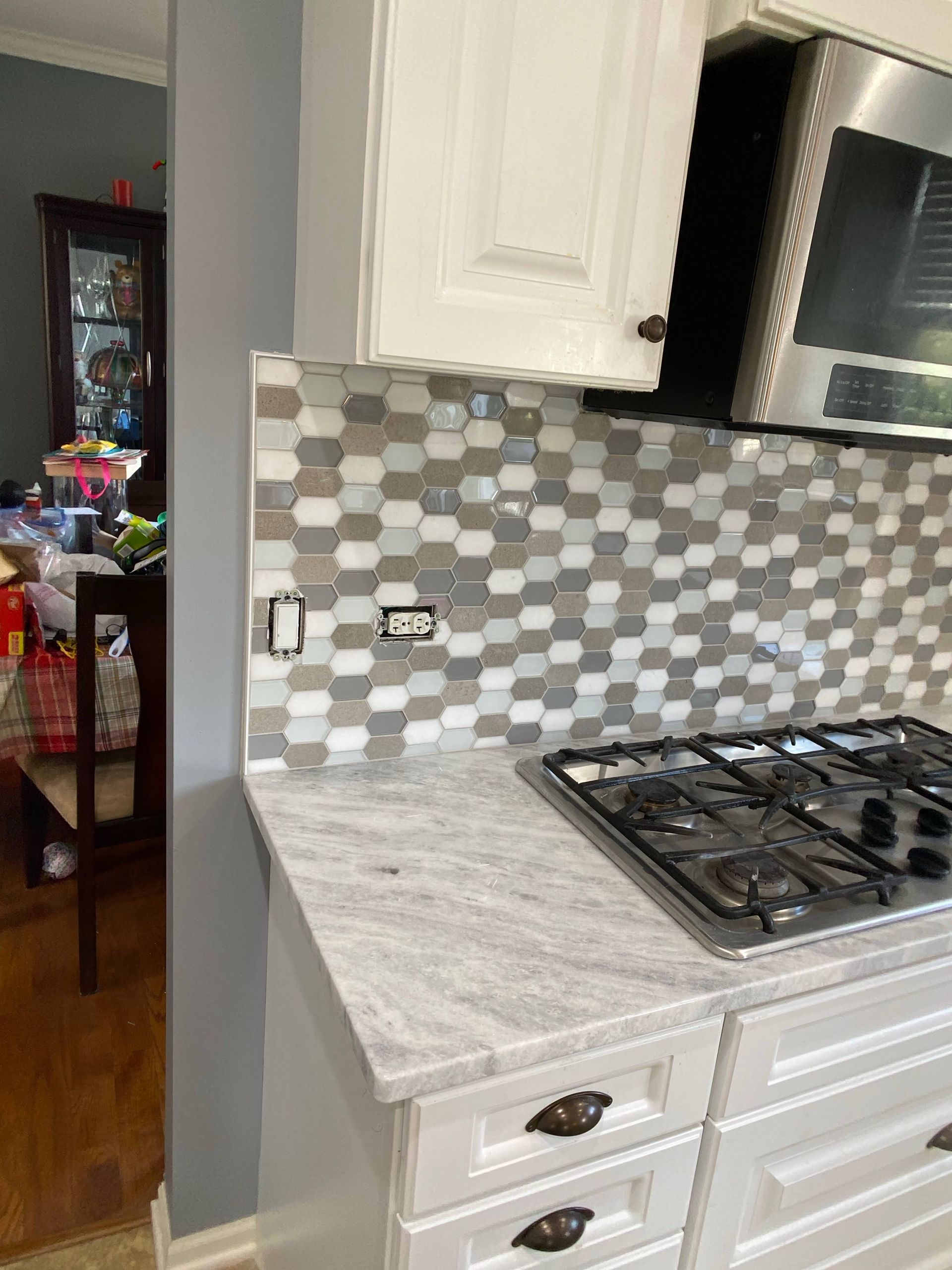 Modern kitchen corner with white cabinets, gray mosaic backsplash, gas cooktop, and marble-look countertop